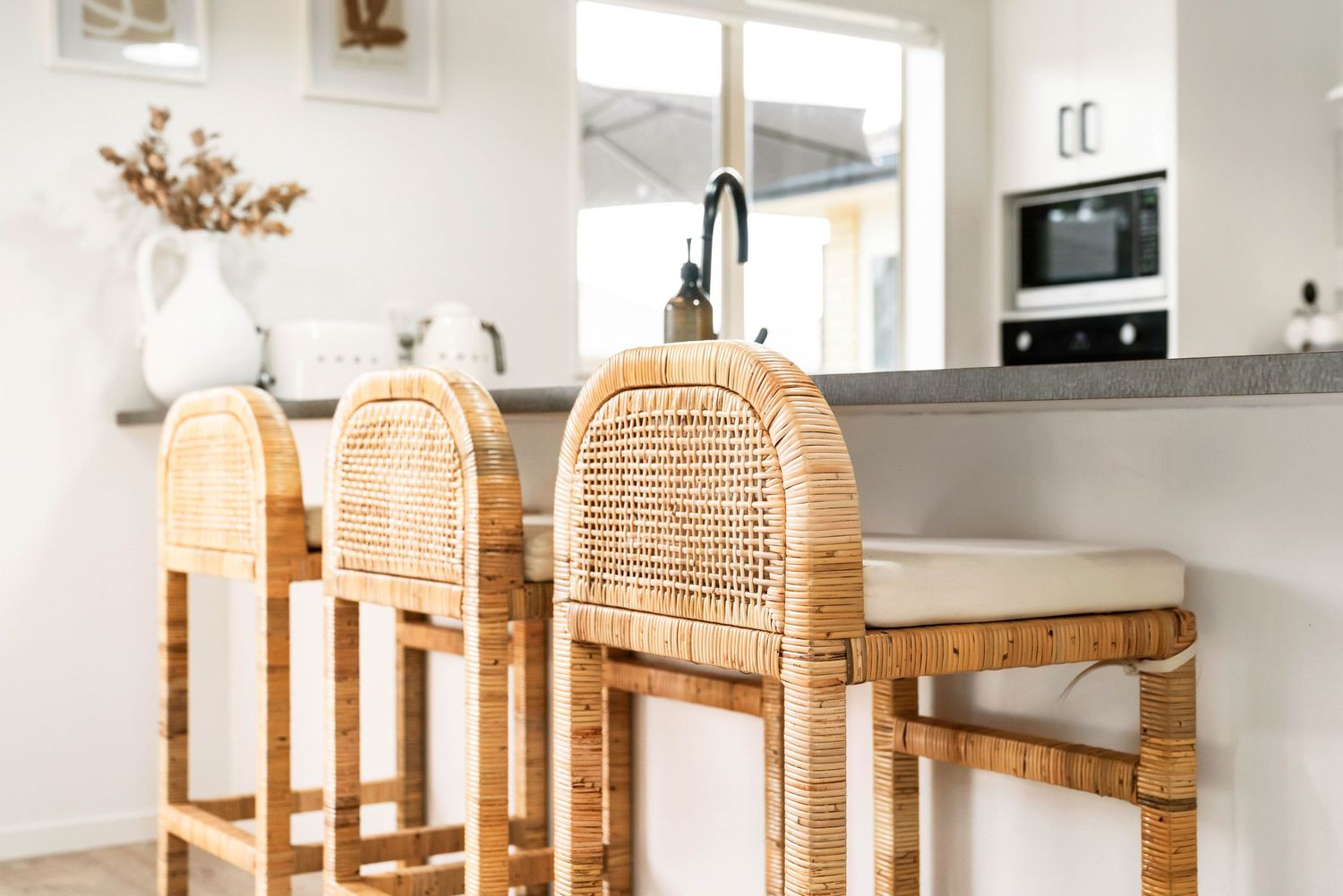 Modern kitchen island with three rattan bar stools and a white vase with dried flowers.