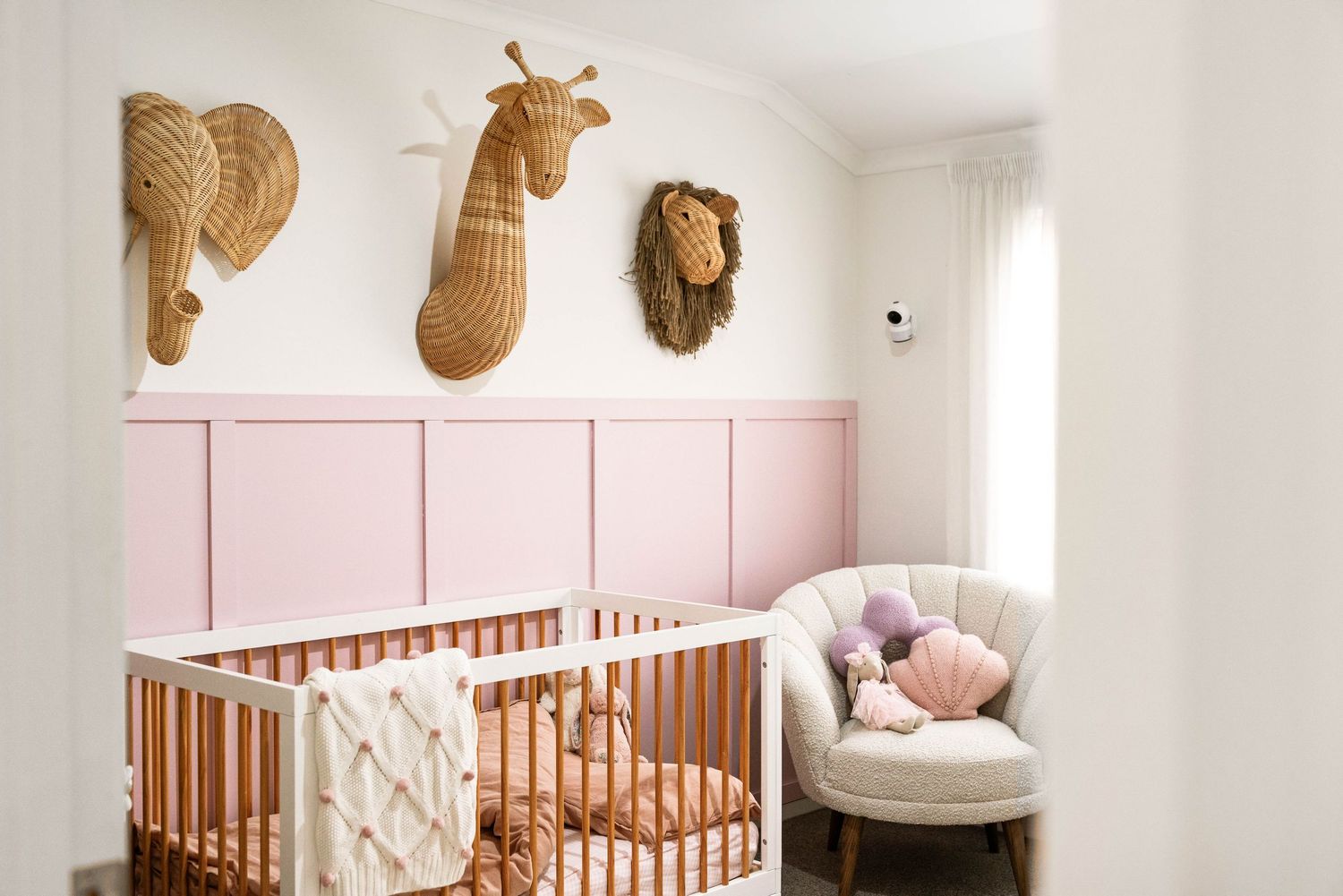 Nursery room with pink walls, wooden crib, and decorative woven baskets mounted on the wall.