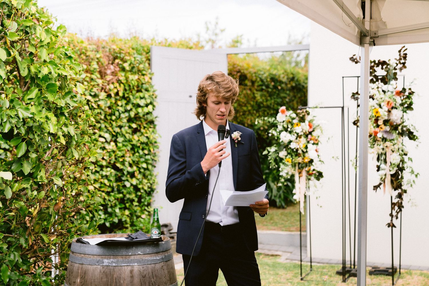 Casual outdoor celebration with wine barrels and greenery under a white tent.