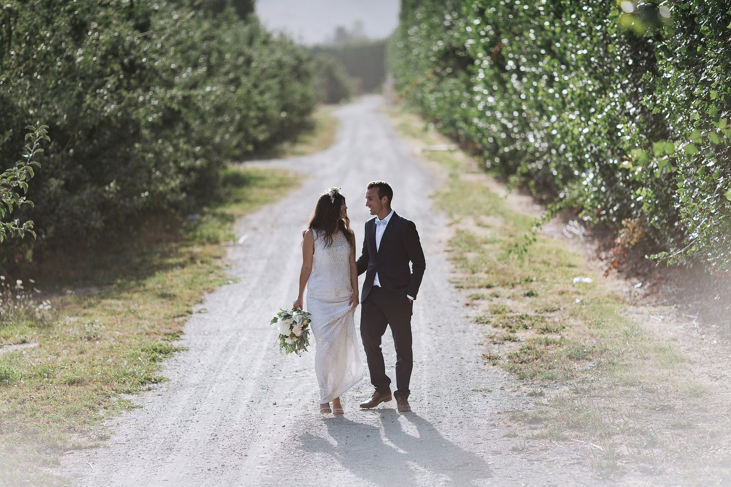 Newlywed couple walks along a serene dirt path surrounded by lush greenery on their wedding day.