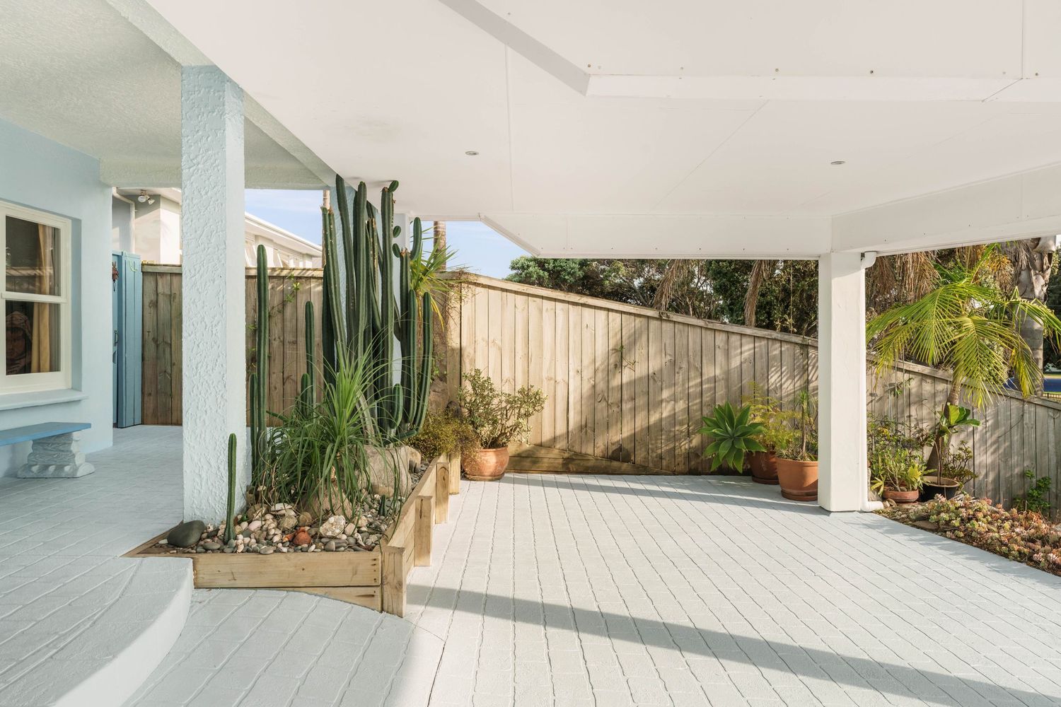 Covered outdoor patio area with desert landscaping featuring tall cacti and white tiled flooring.