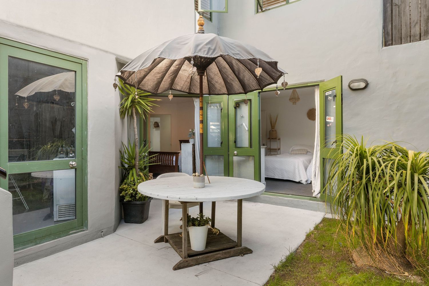 Outdoor patio space with umbrella table and tropical plants near glass sliding doors.
