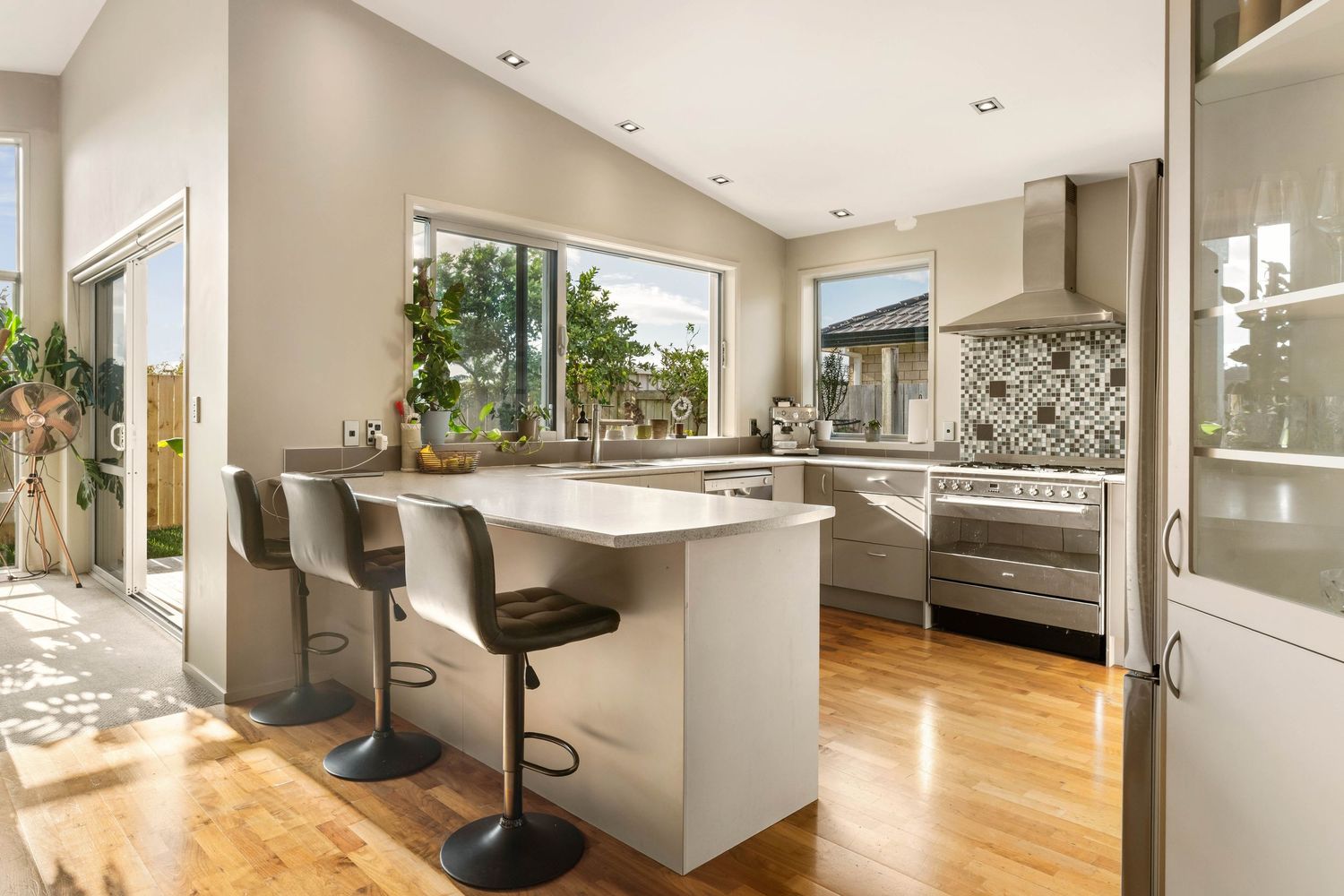 Contemporary open kitchen with white quartz countertops, bar seating and patterned backsplash flooded with natural light.
