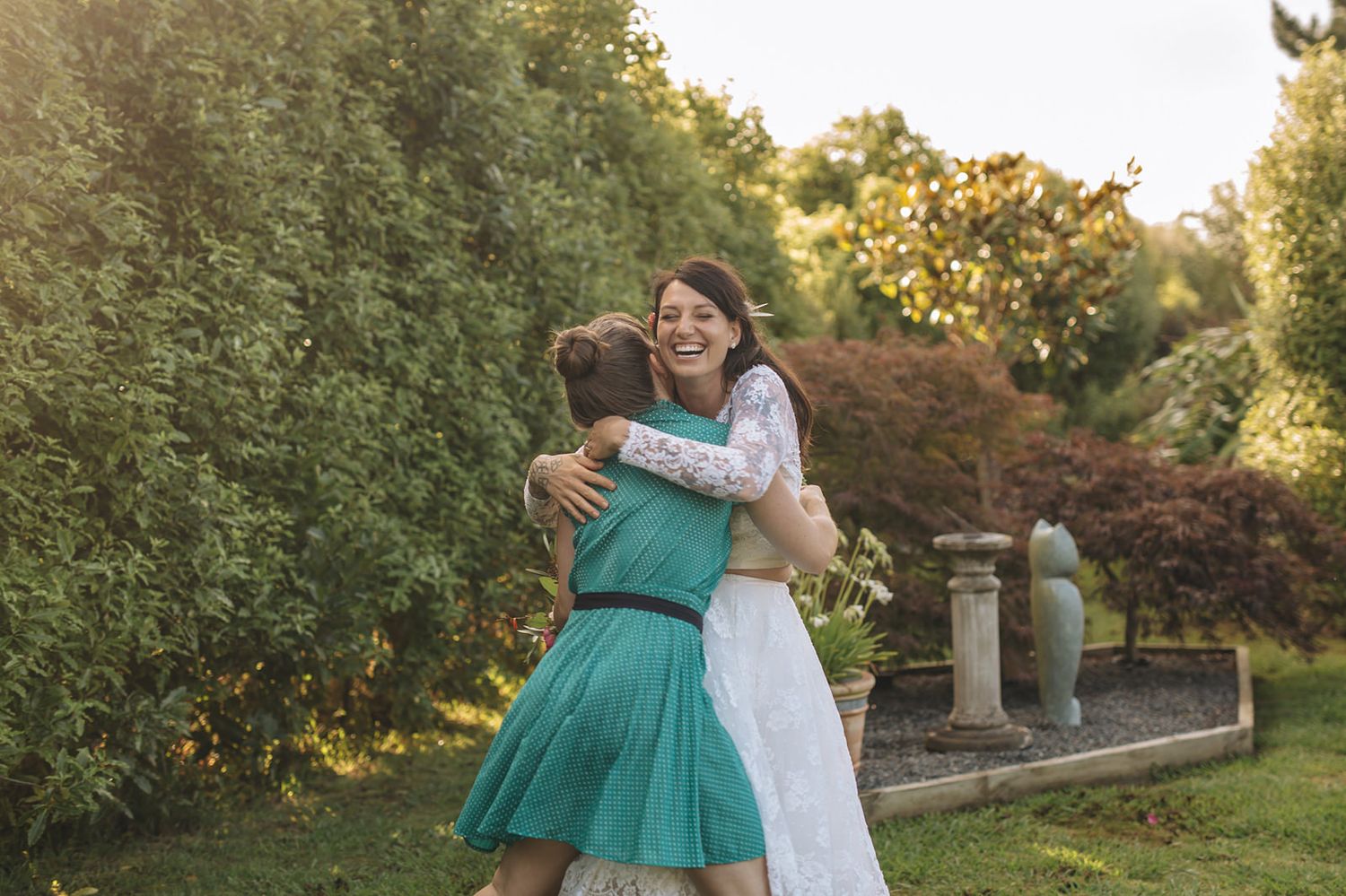 A casual outdoor photo session in a lush garden at sunset with two individuals embracing in coordinating white and green outfits.