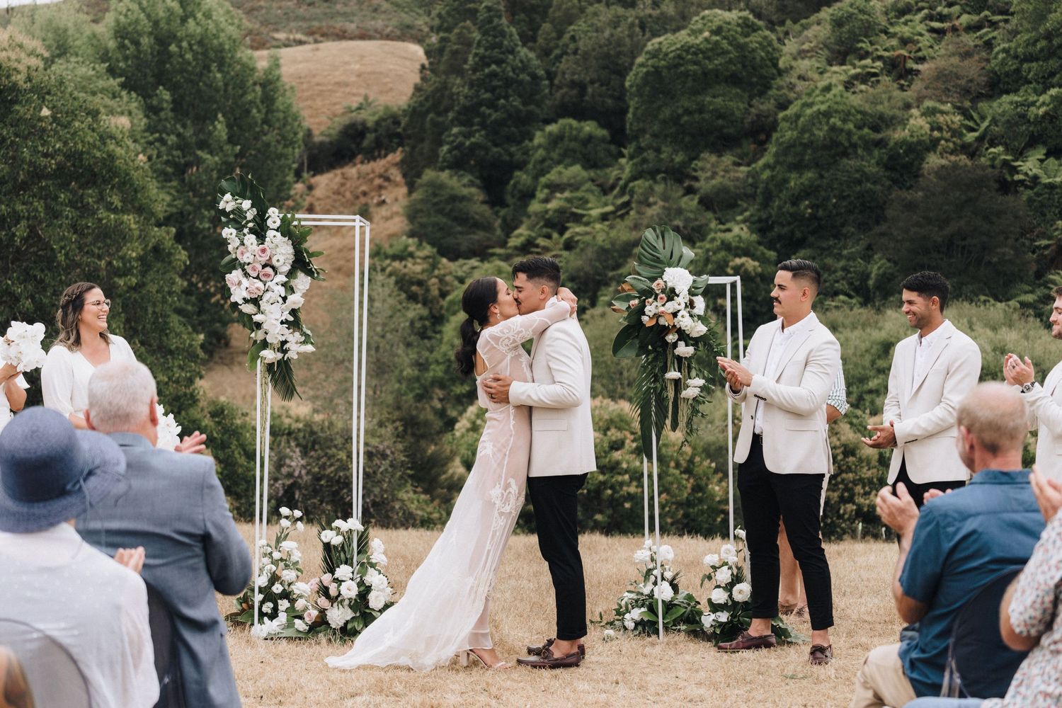 Wedding ceremony moment in scenic outdoor setting with floral arch and mountain backdrop.