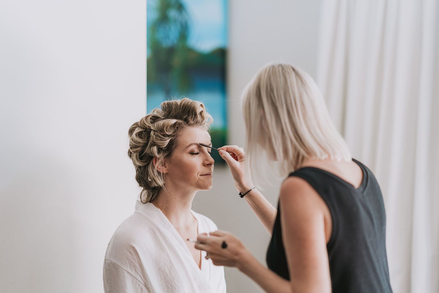 Makeup artist applies cosmetics to bride during wedding preparation, creating a glamorous bridal look.