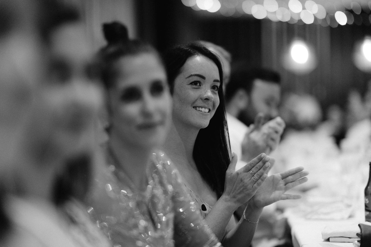 A blurred black and white panoramic montage showing people at a formal event with bokeh lights in the background.