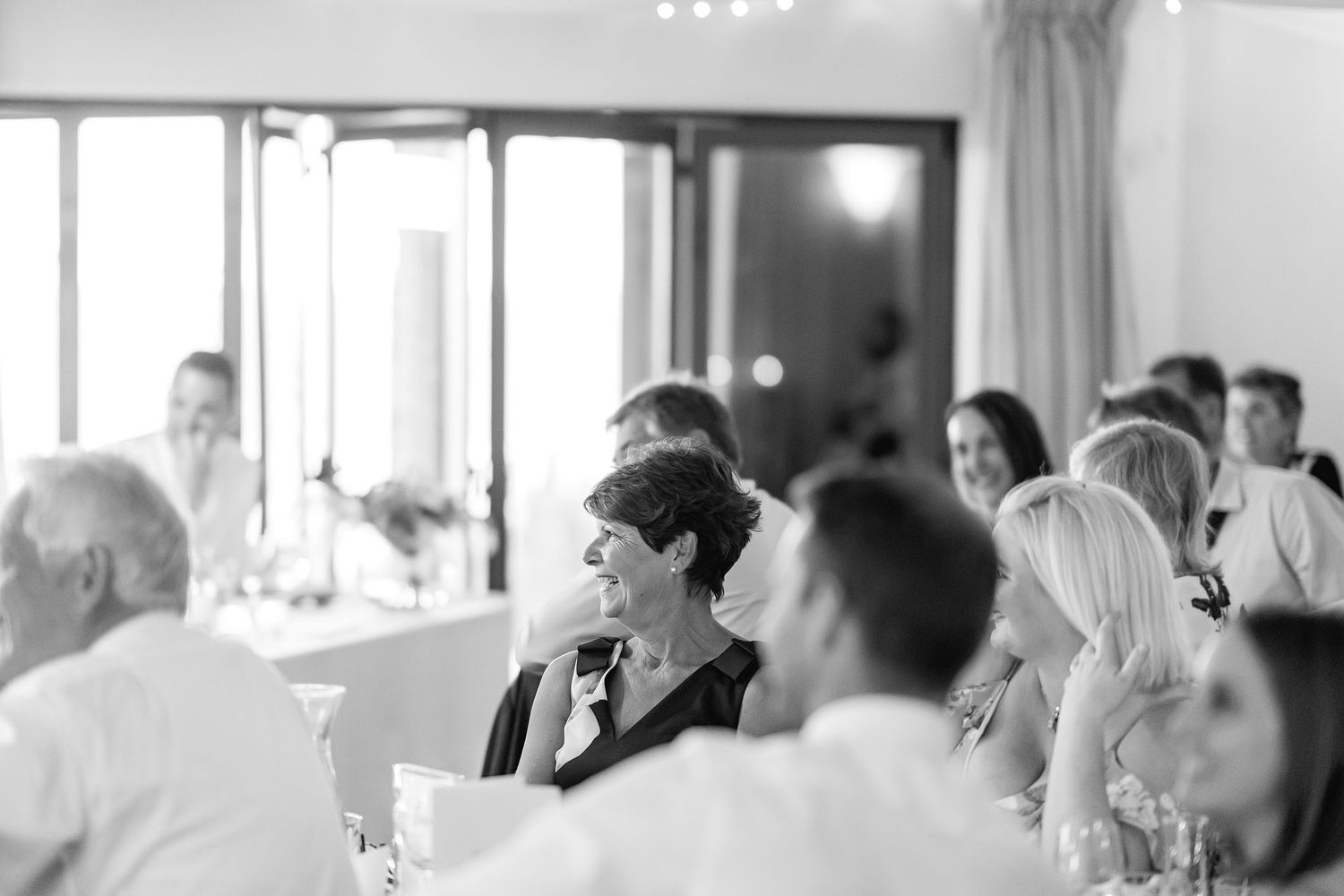 A black and white photograph showing people gathered at tables during a social event or reception.