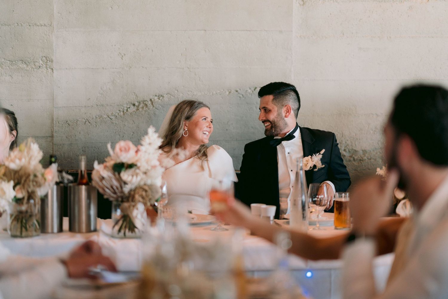 Couple shares intimate moment at reception dinner table decorated with floral centerpieces.