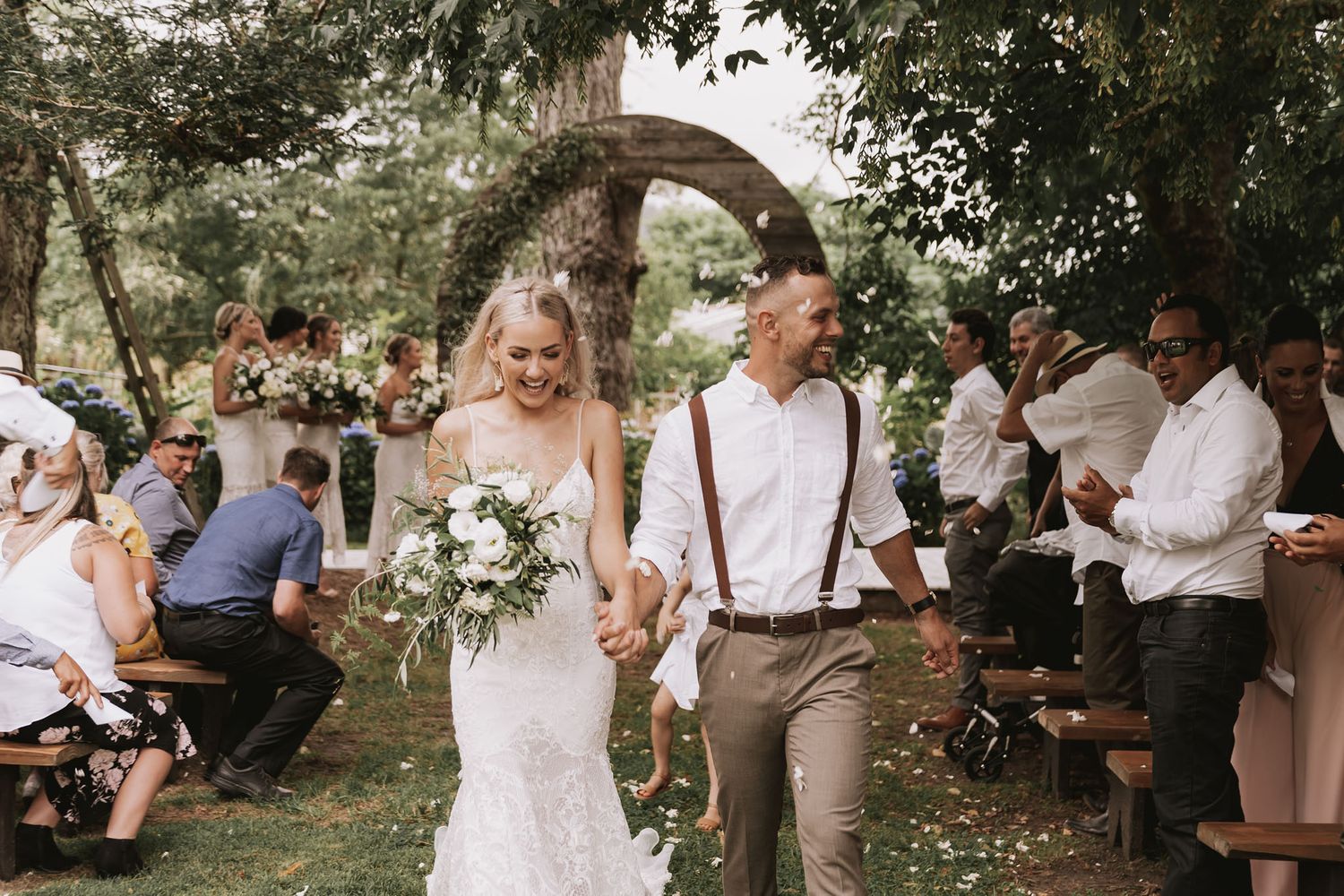 A joyful couple walks down the aisle during their rustic outdoor wedding celebration with guests seated on benches.