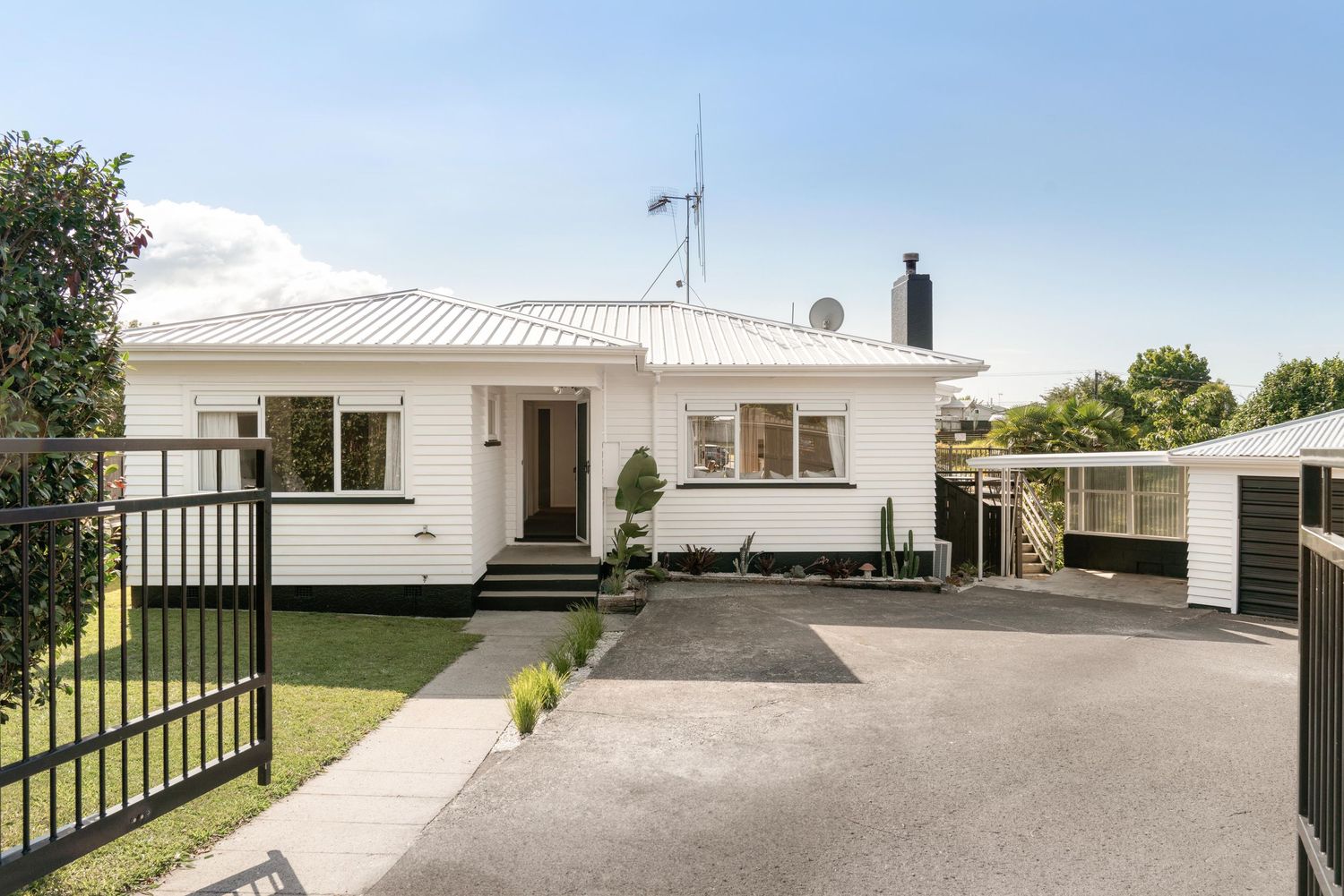 Modern white single-story ranch home with multiple driveways and lush green lawn surrounded by landscaping.