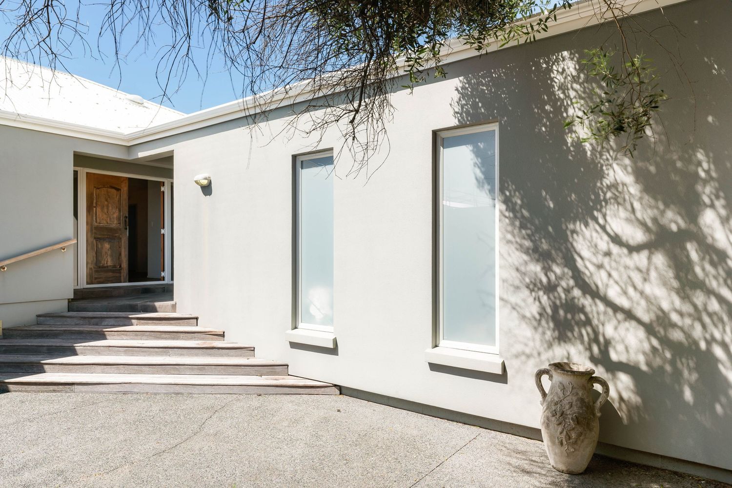 Contemporary white stucco house exterior with concrete steps and frosted windows.