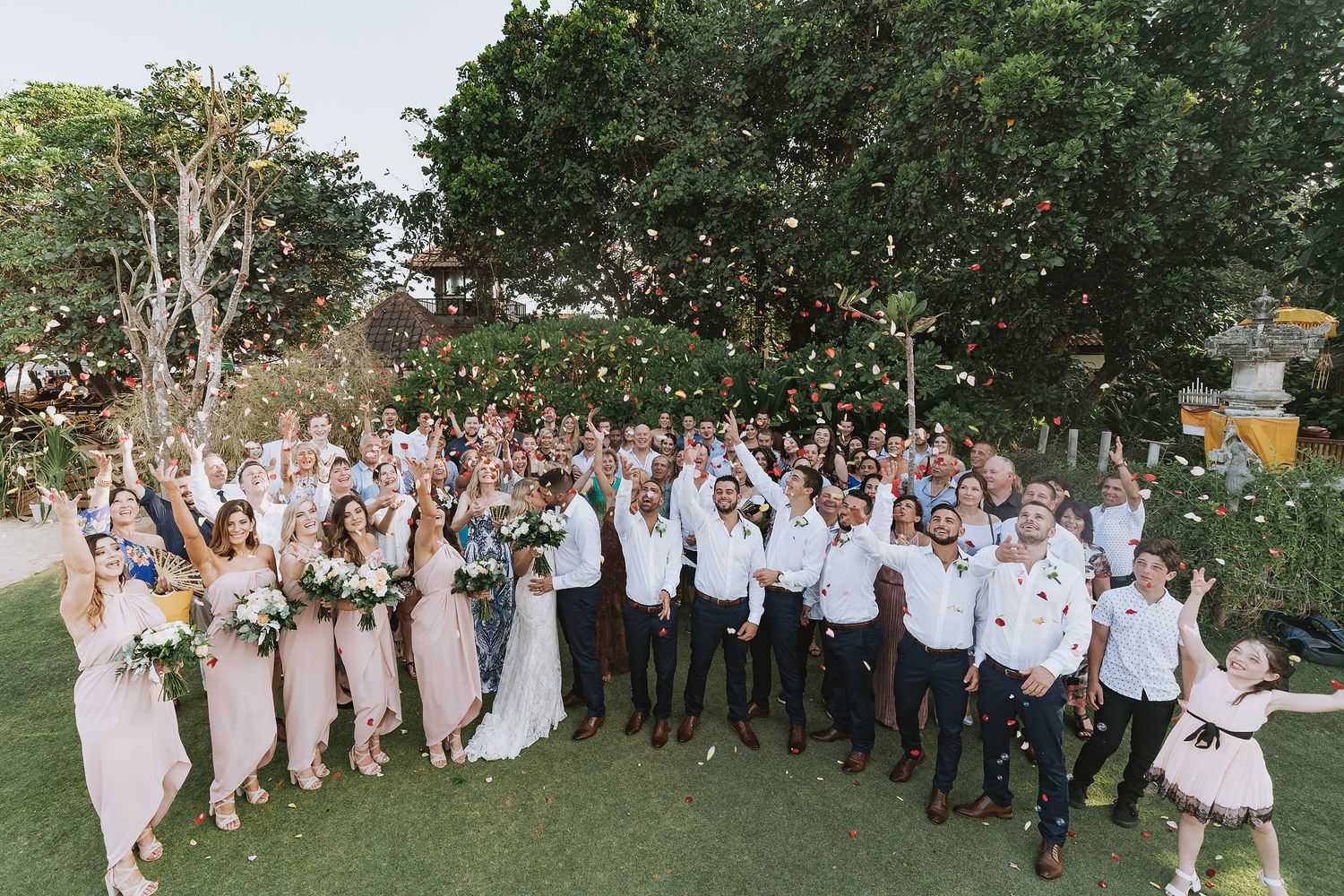 Large wedding party stands together for group photos on a lush green lawn during an outdoor celebration.