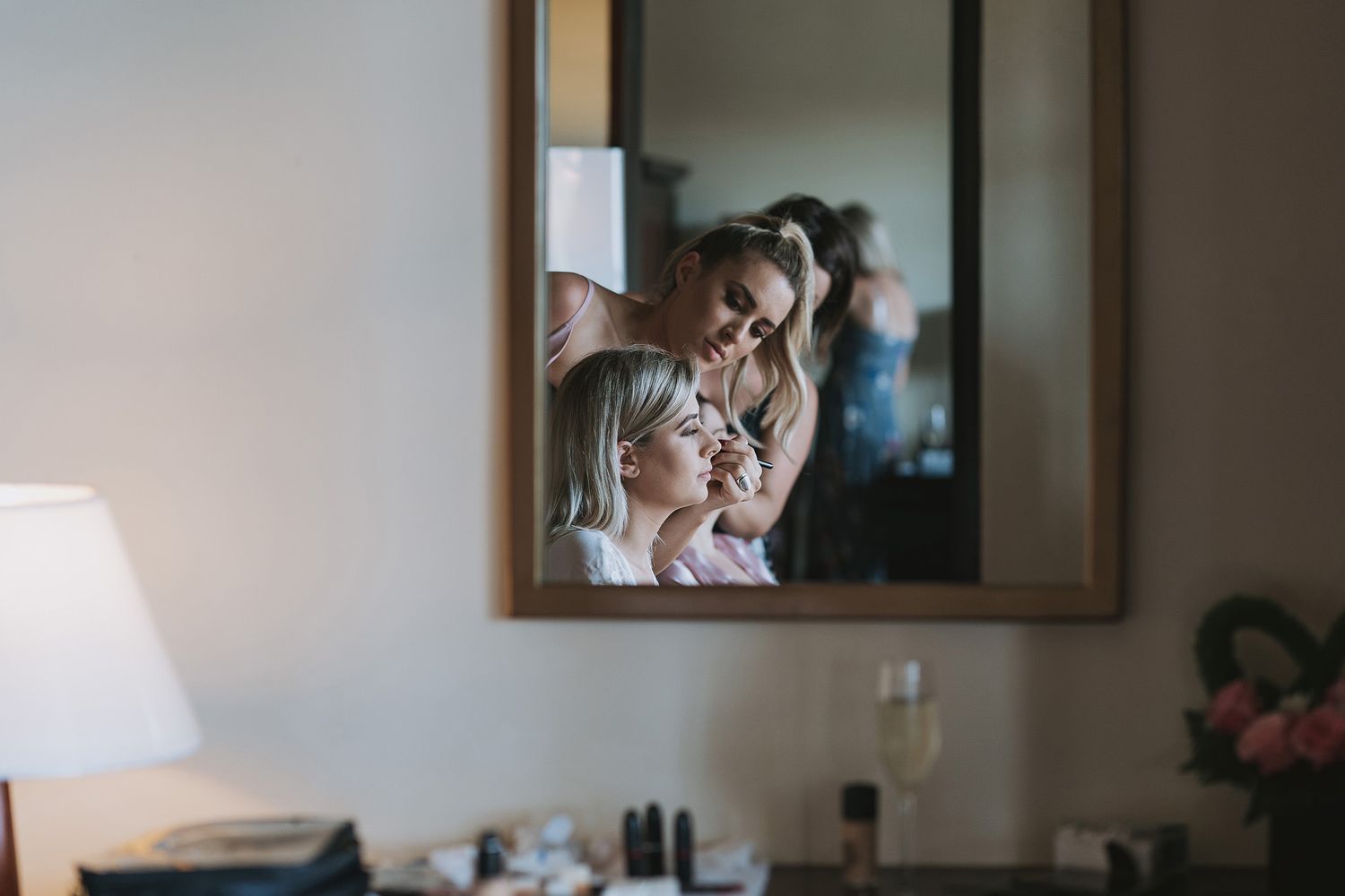 A reflection in a mirror shows a person getting ready with styling tools in a brightly lit room.