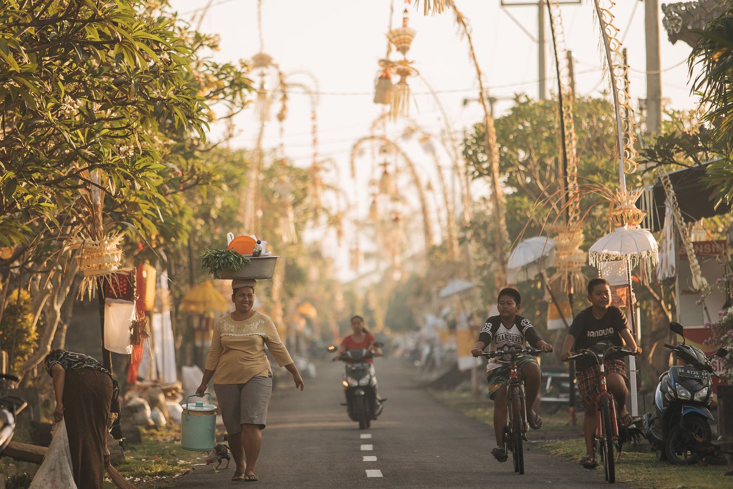 People cycling and walking down a palm tree-lined street in Bali at sunset with warm golden lighting.
