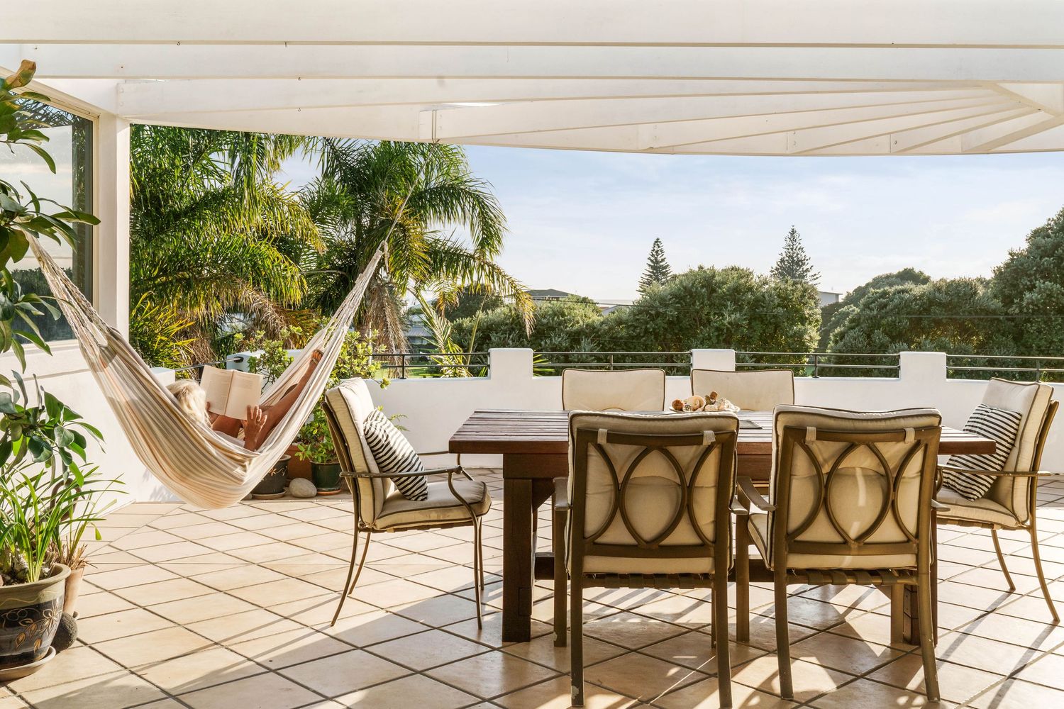 Inviting outdoor patio with hammock and dining furniture overlooking tropical landscaping and palm trees.