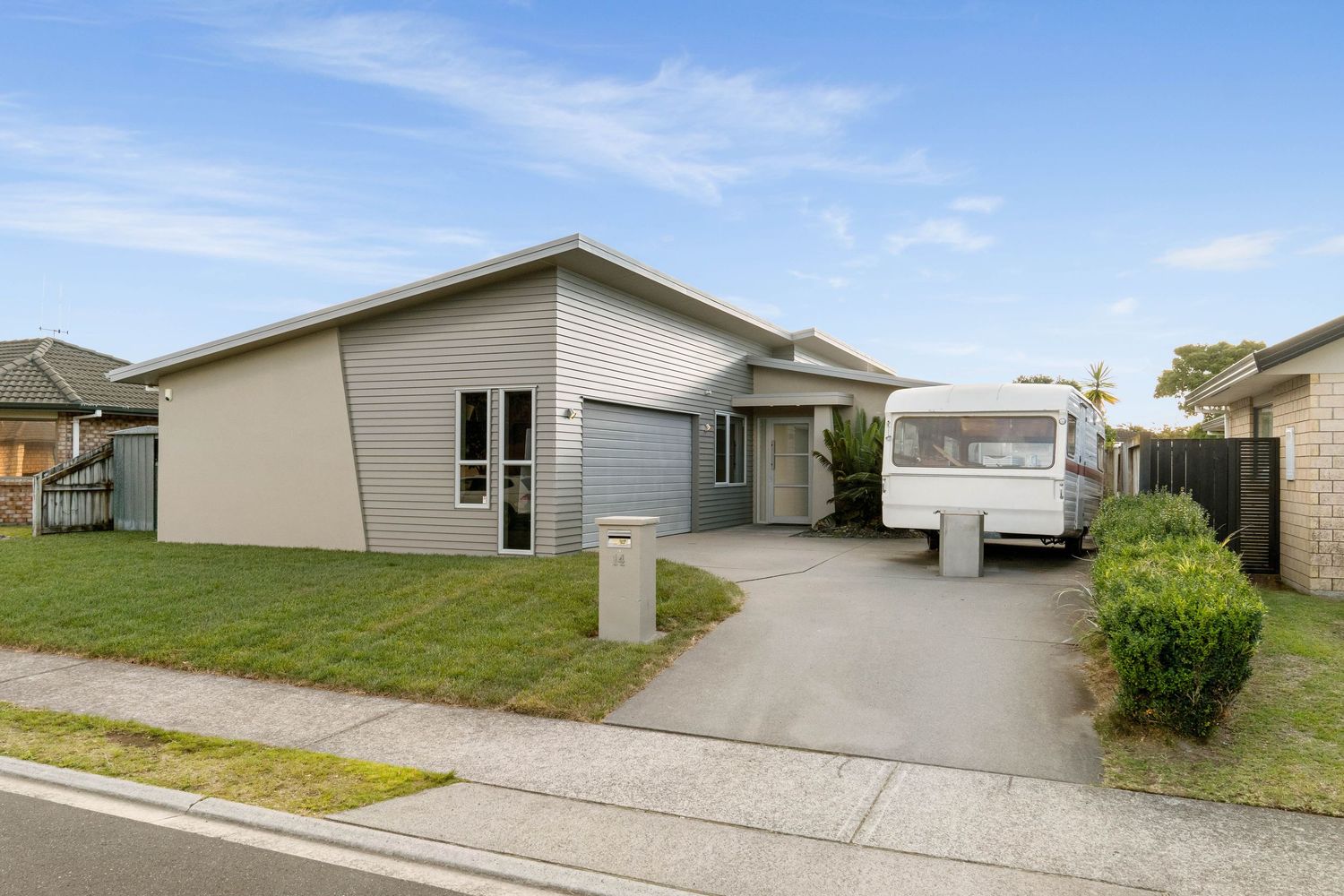 Modern single-story beige house with caravan driveway and small front lawn on a suburban street.