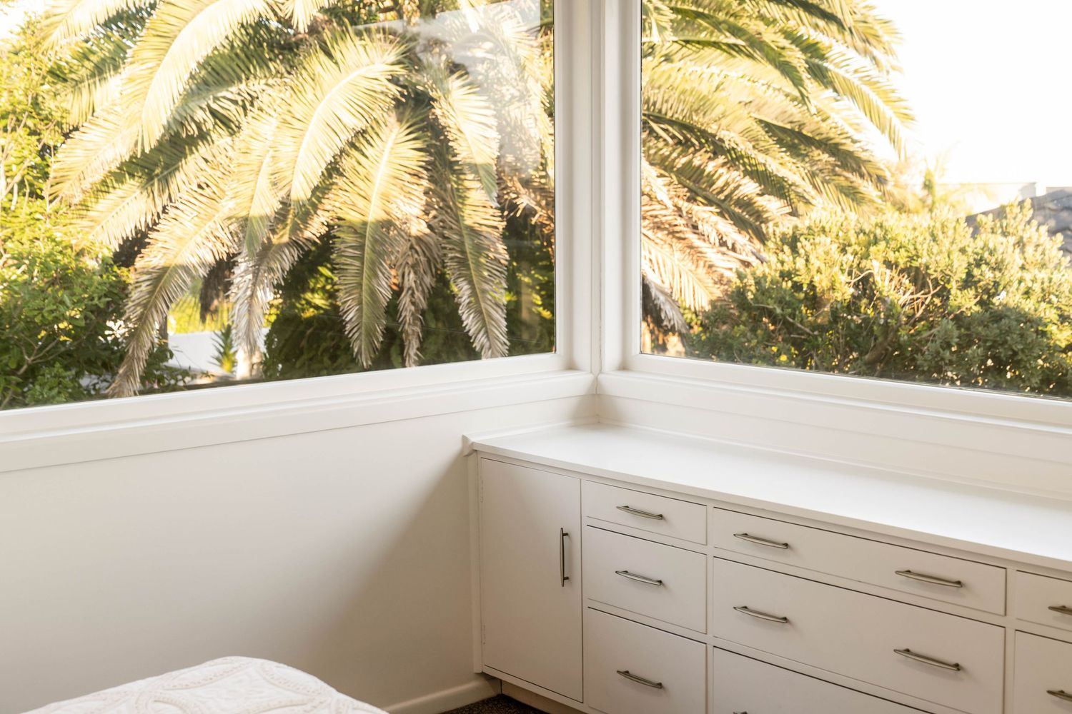 Palm tree framed bedroom windows with white built-in storage and modern furnishings.