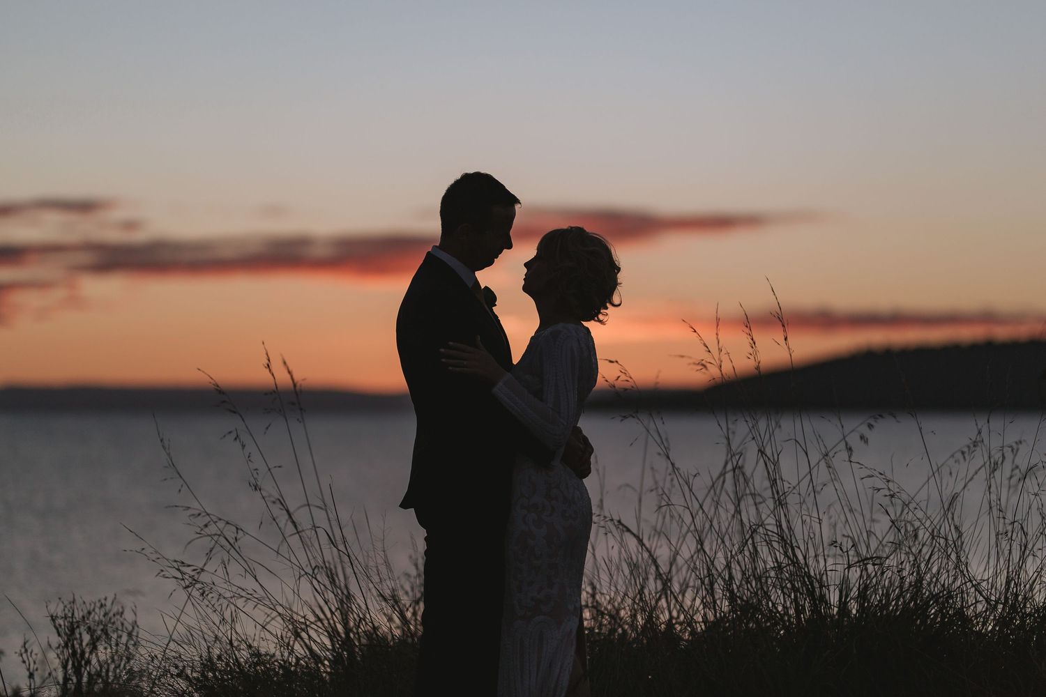 Silhouettes of a couple against a vibrant sunset sky over the water, creating a romantic and peaceful atmosphere.