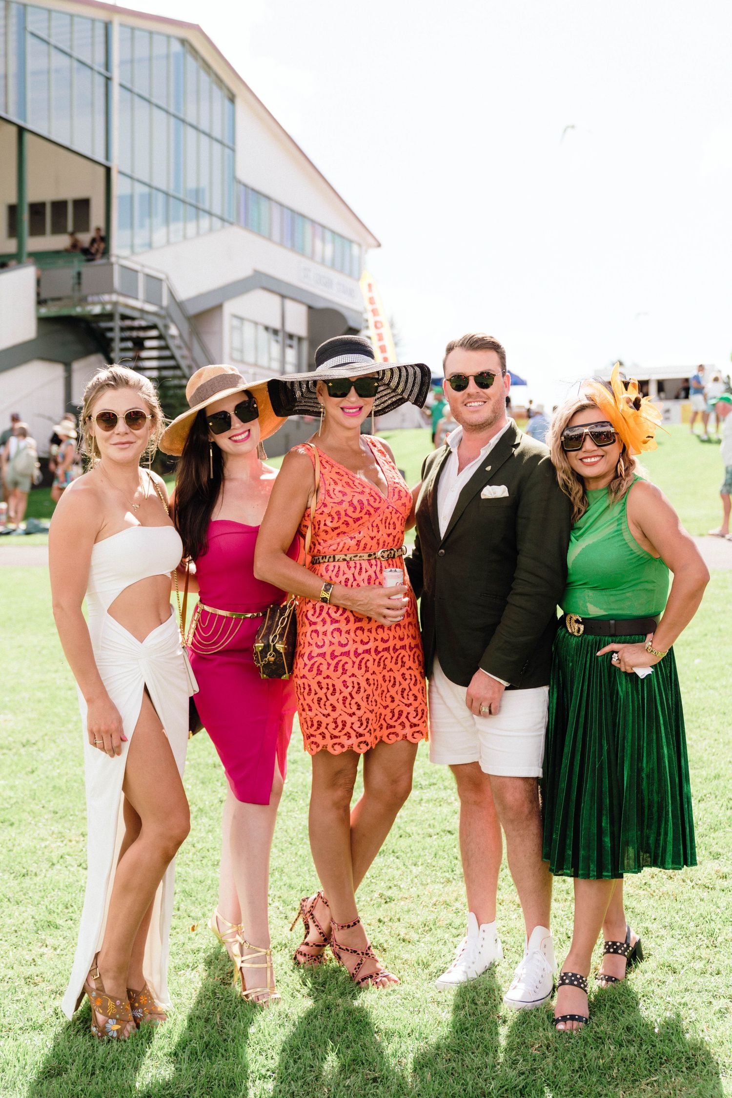 A group in colorful summer dresses and sunhats poses on a grassy lawn.