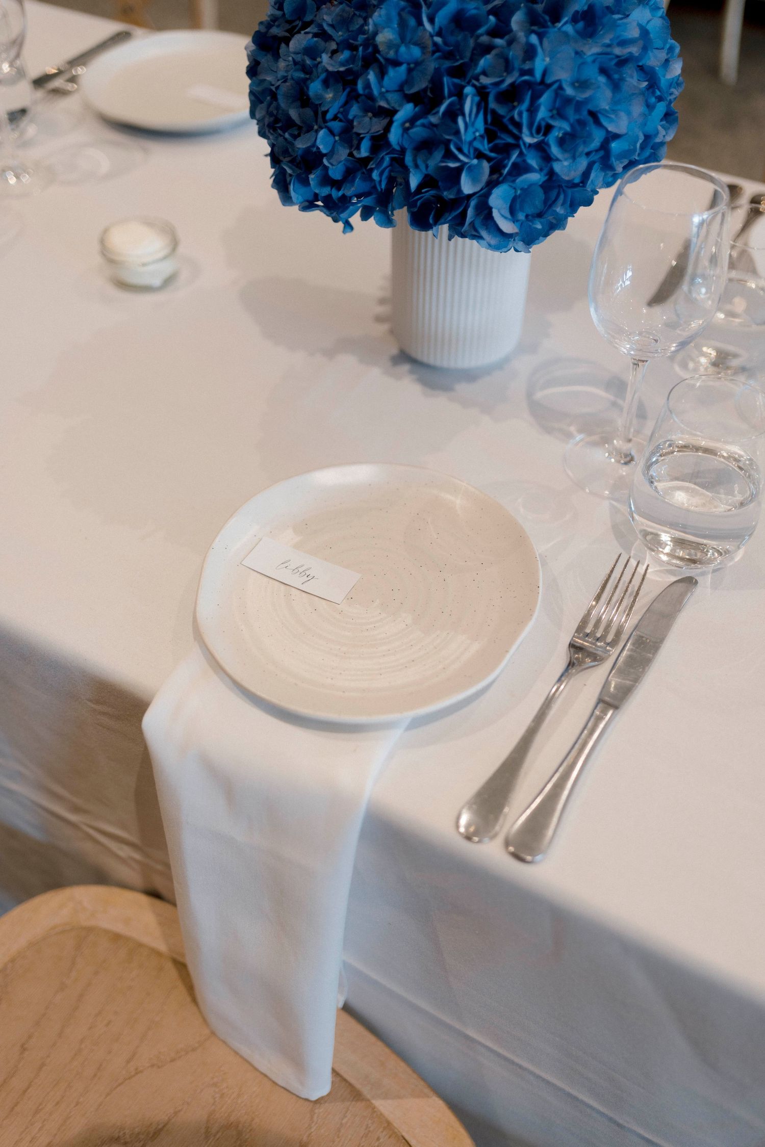 Elegant table setting with bright blue hydrangea centerpiece, white plates, and crystal glassware.
