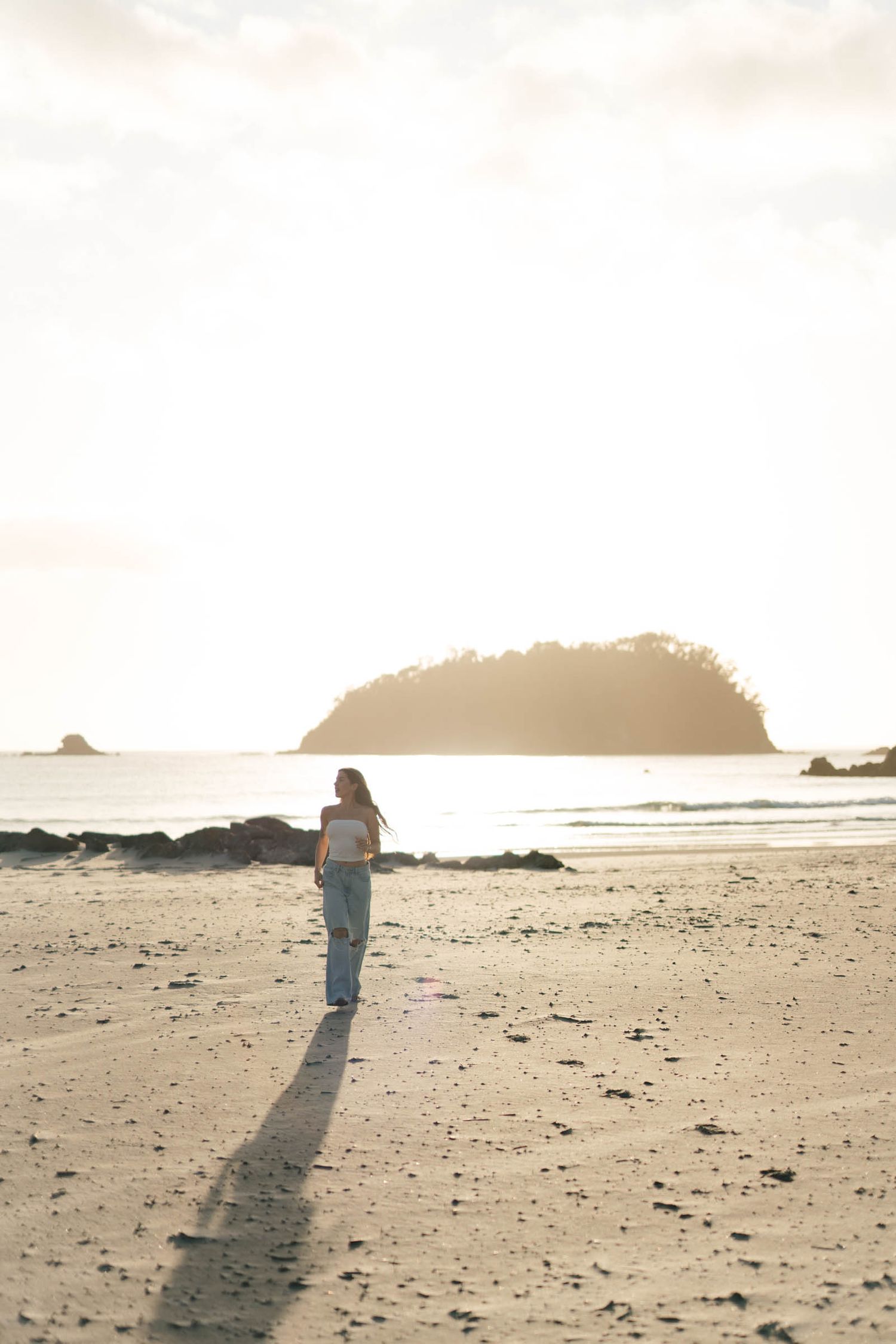 Silhouette of person walking on beach with island visible in background at sunset.