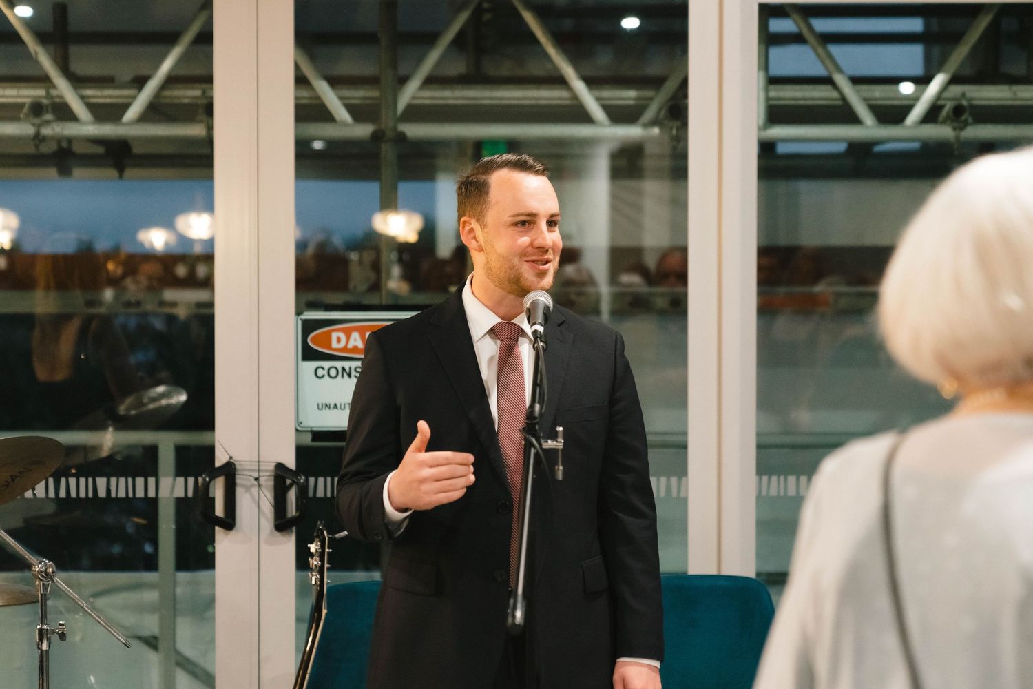 Speaker addressing audience at an elegant indoor event venue with large windows.