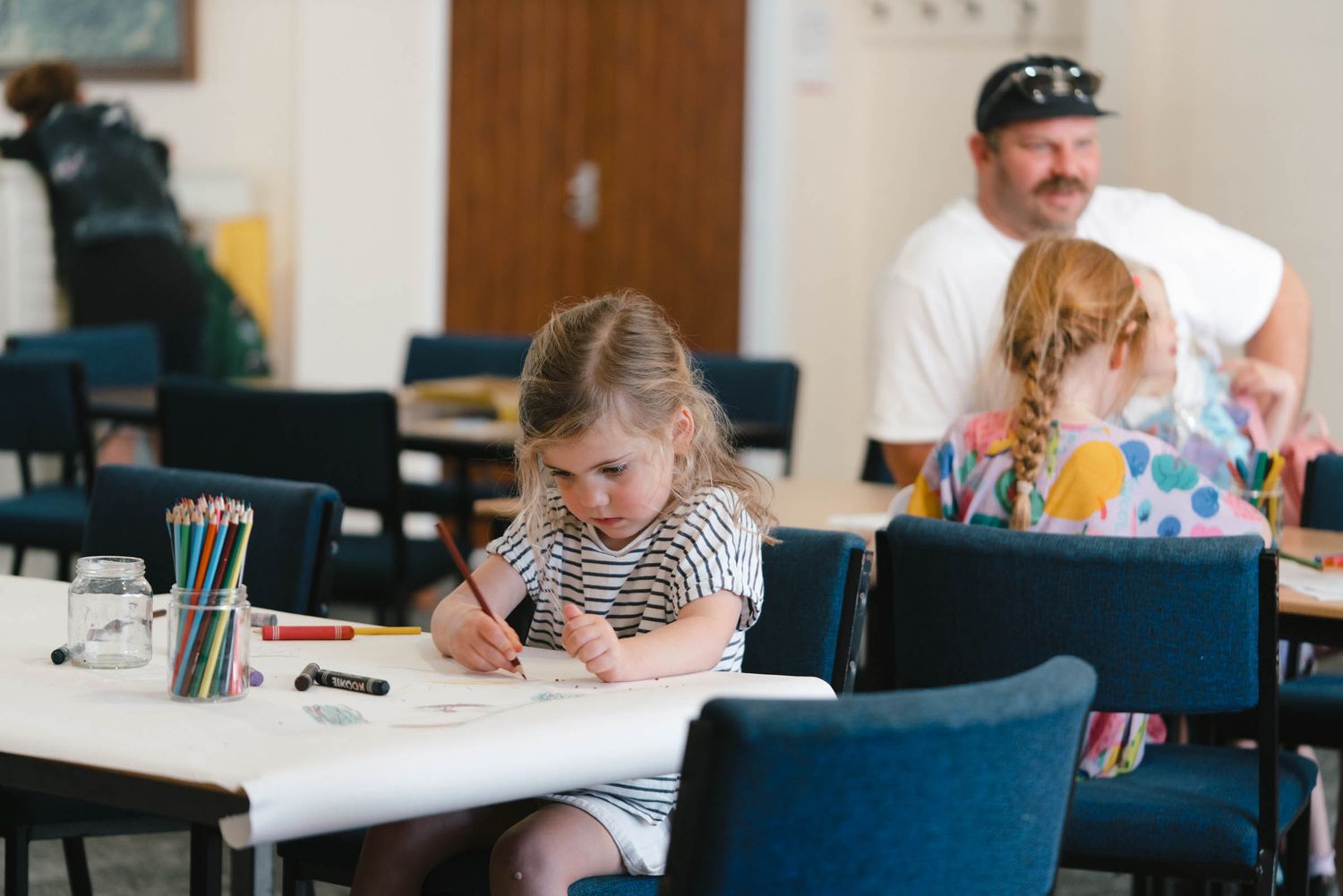 Children sitting at tables with art supplies during a community activity.