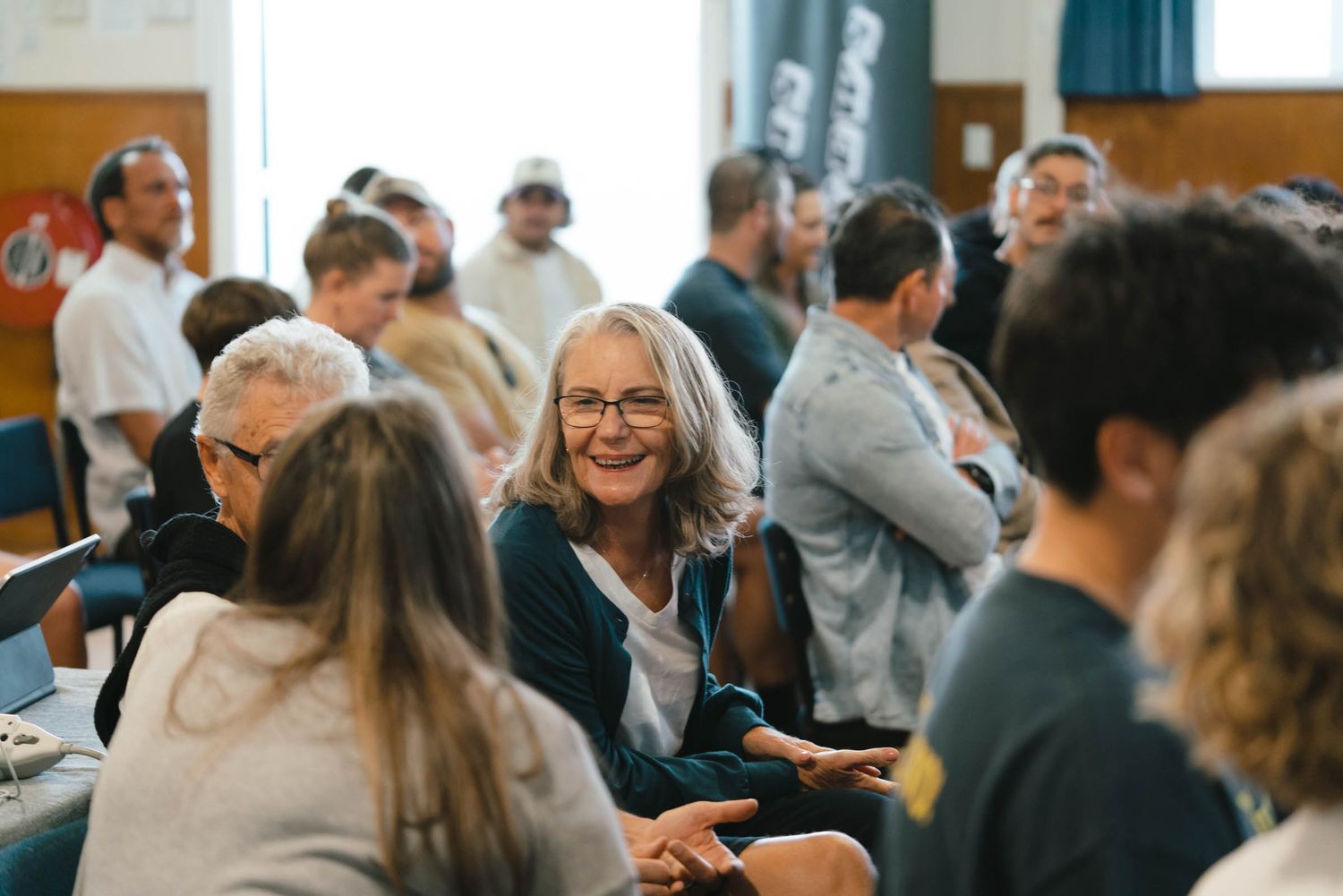 Diverse group of people gathered in conversation at a community meeting or social event.