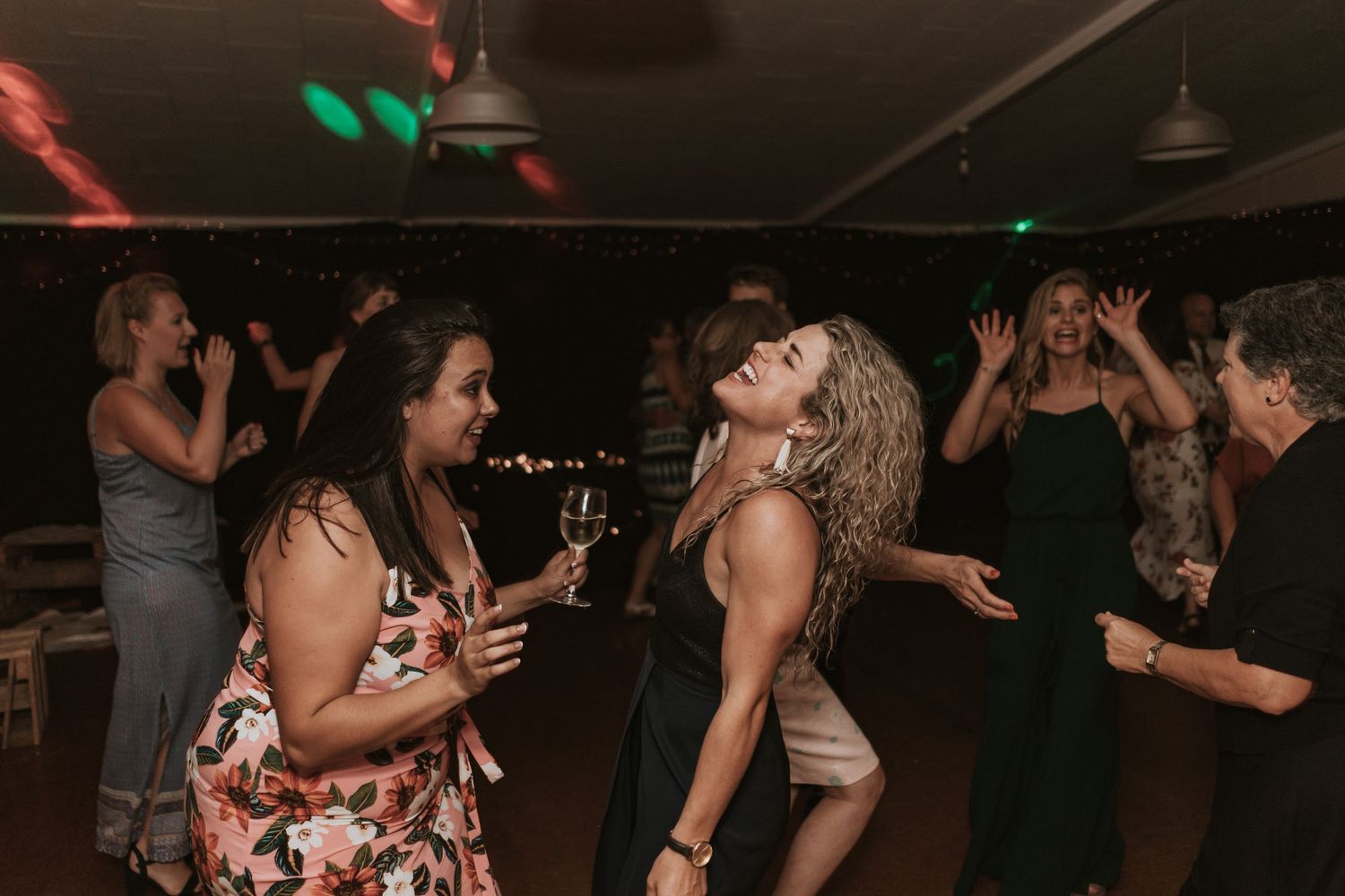 People dancing and socializing in a dimly lit nightclub setting with colorful lighting effects.