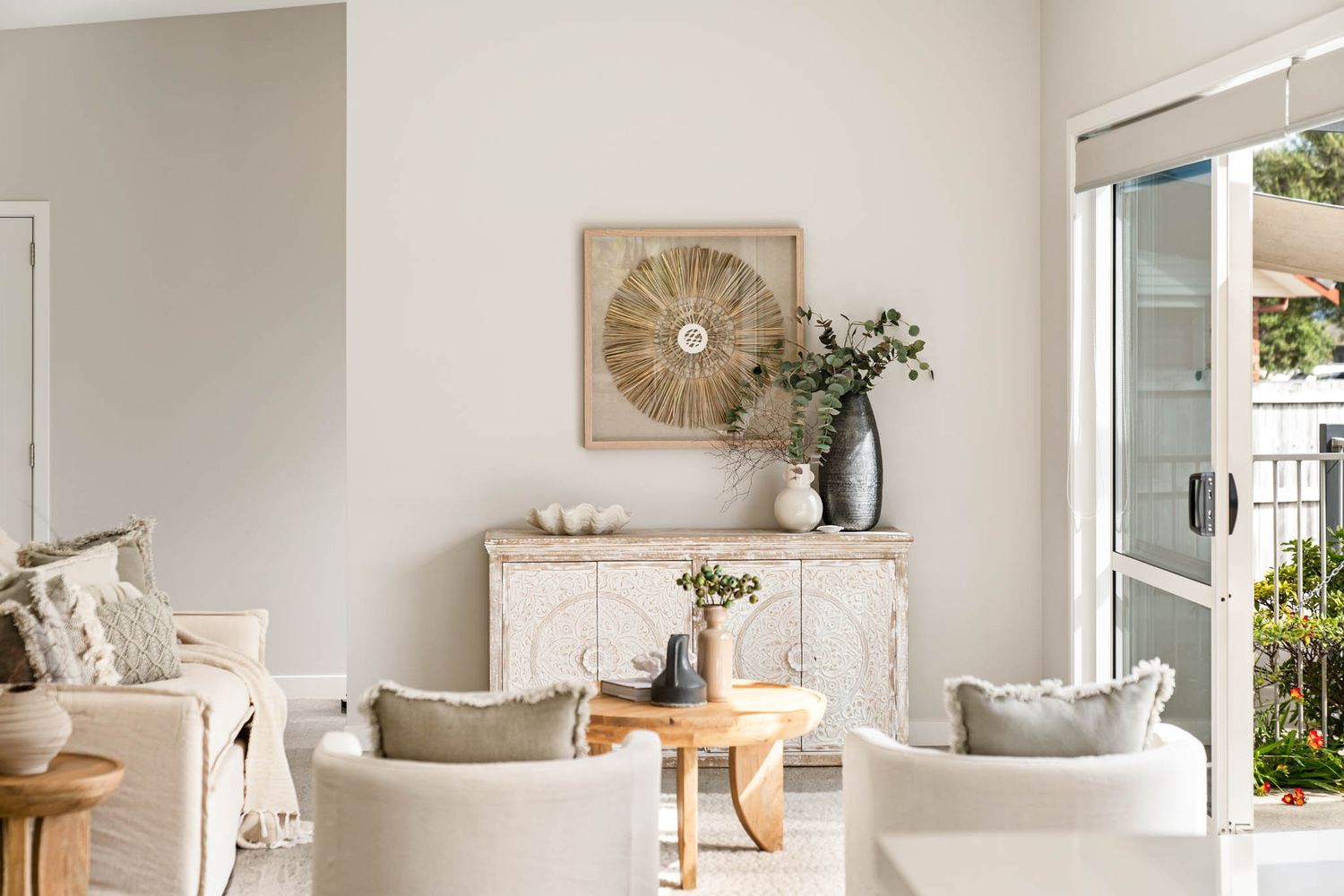 A bright coastal living room with white furniture, natural wood accents and decorative wall art in beige tones.