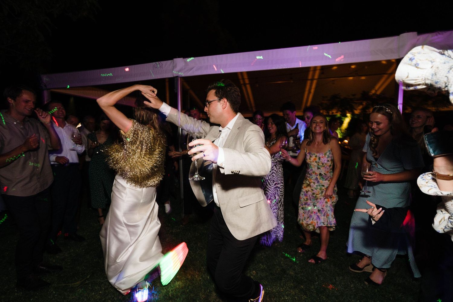People dancing together at a nighttime wedding reception celebration with purple lighting and festive atmosphere.