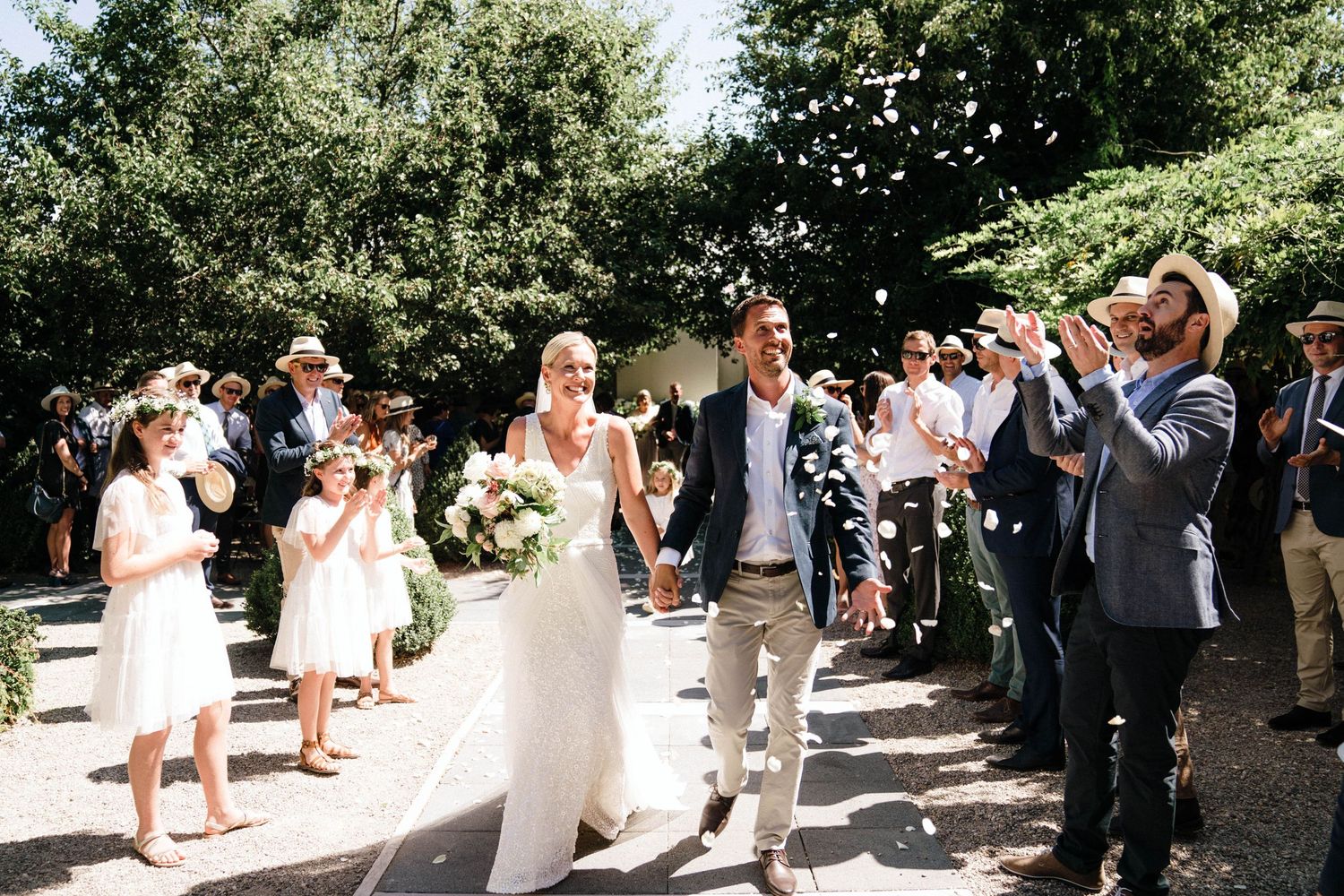 Wedding guests taking photos with their phones as newlyweds walk down an outdoor garden path in summer.