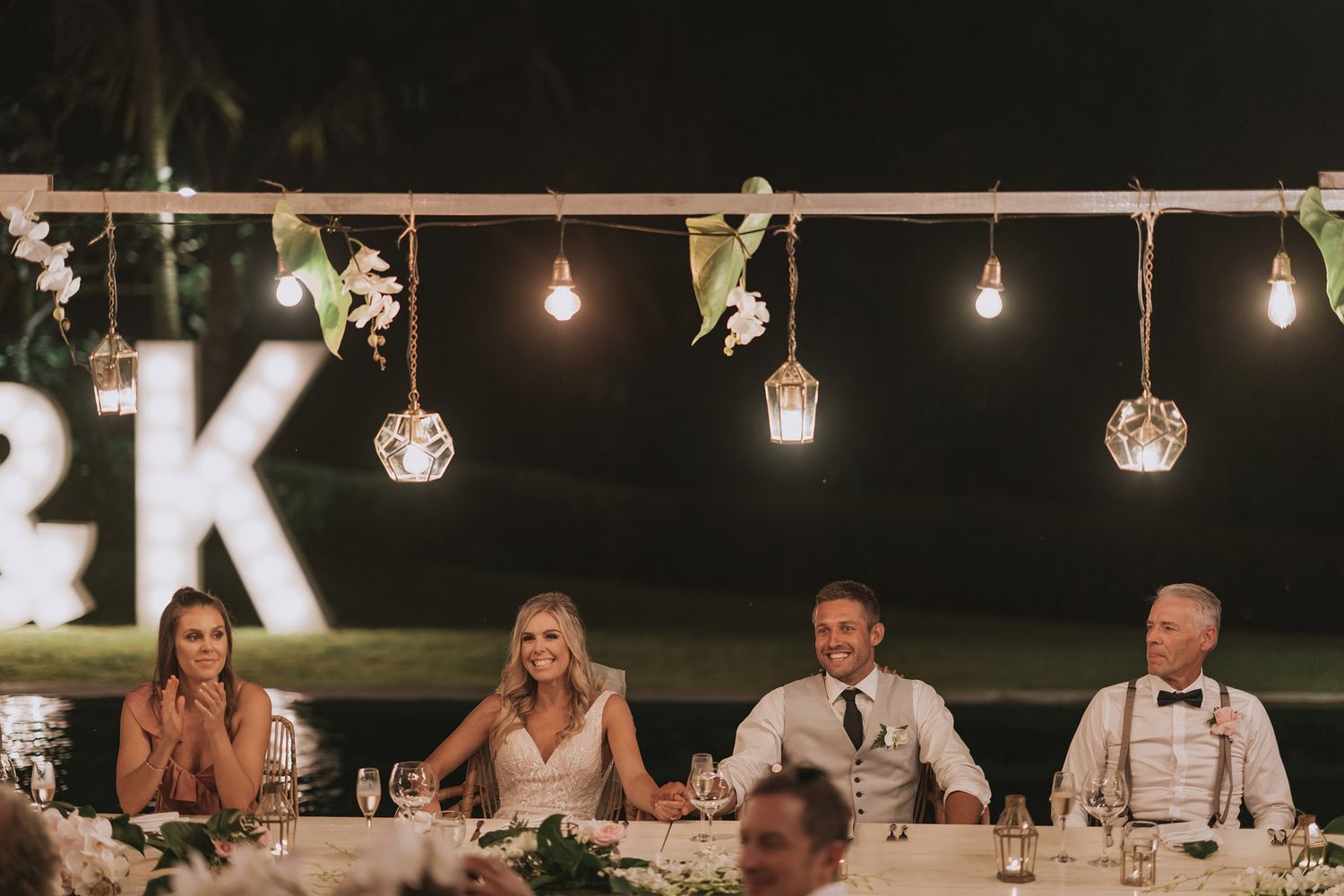 Long reception table decorated with string lights and rustic decor for outdoor wedding celebration.