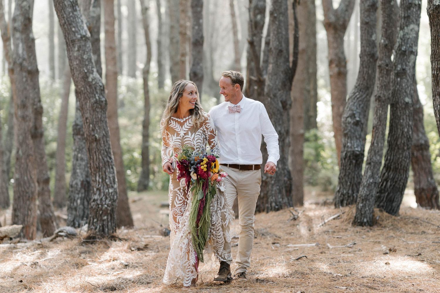 A couple stands together in misty woods while holding a vibrant floral bouquet in a romantic photoshoot.