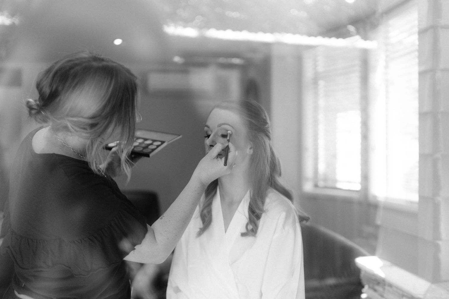 A makeup artist applies cosmetics to a client in a brightly lit room during a beauty session.