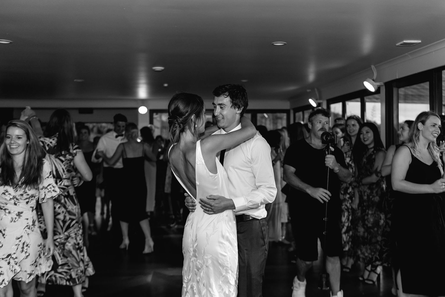 Black and white photo of couples slow dancing at an indoor wedding reception venue.