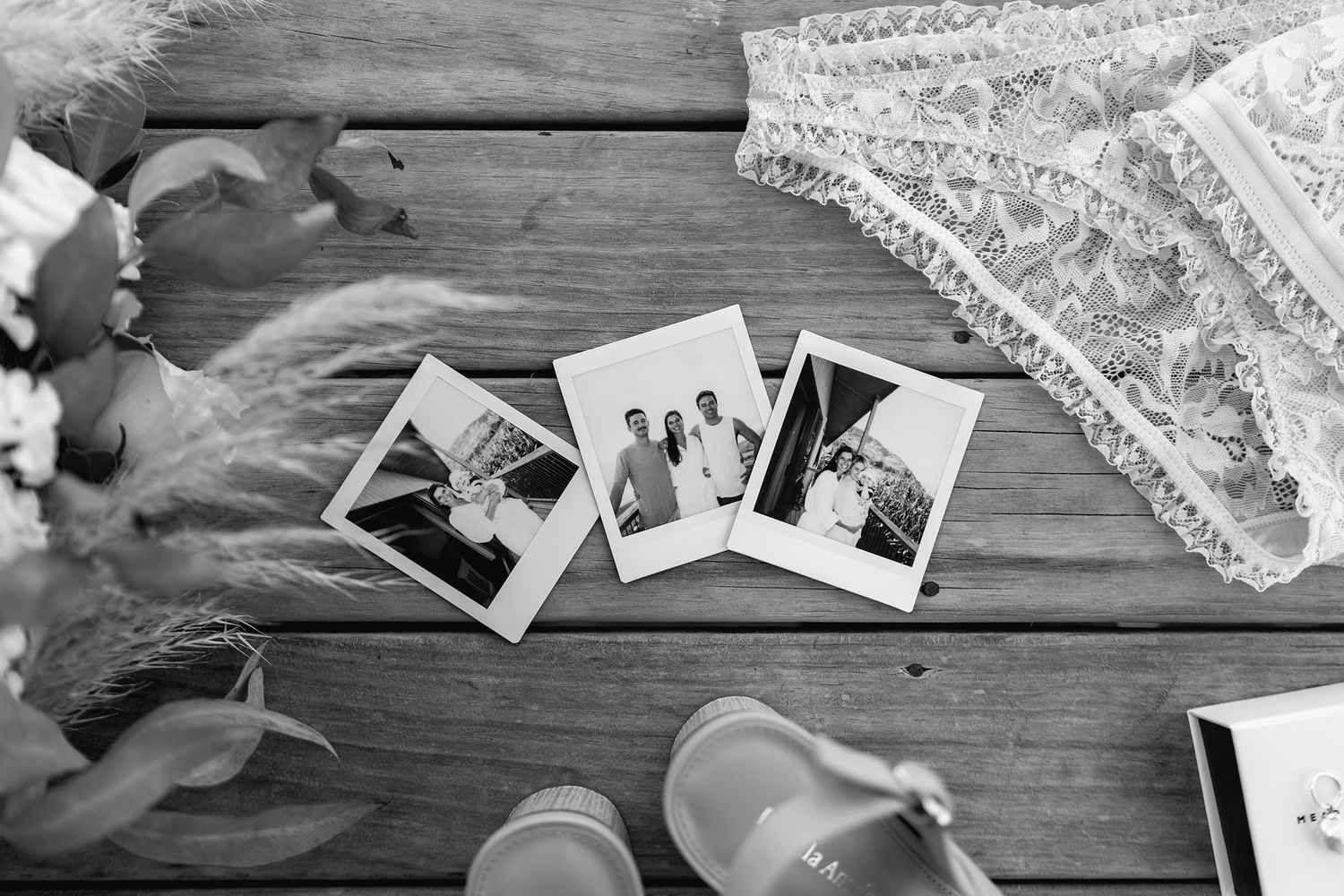 Black and white photograph of vintage photos scattered on wooden table with lace fabric and ballet shoes.