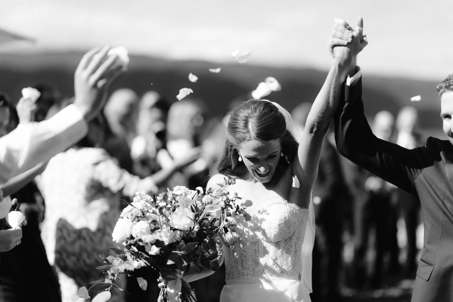 Joyful outdoor celebration with raised hands and bouquet of flowers captured in black and white photography.