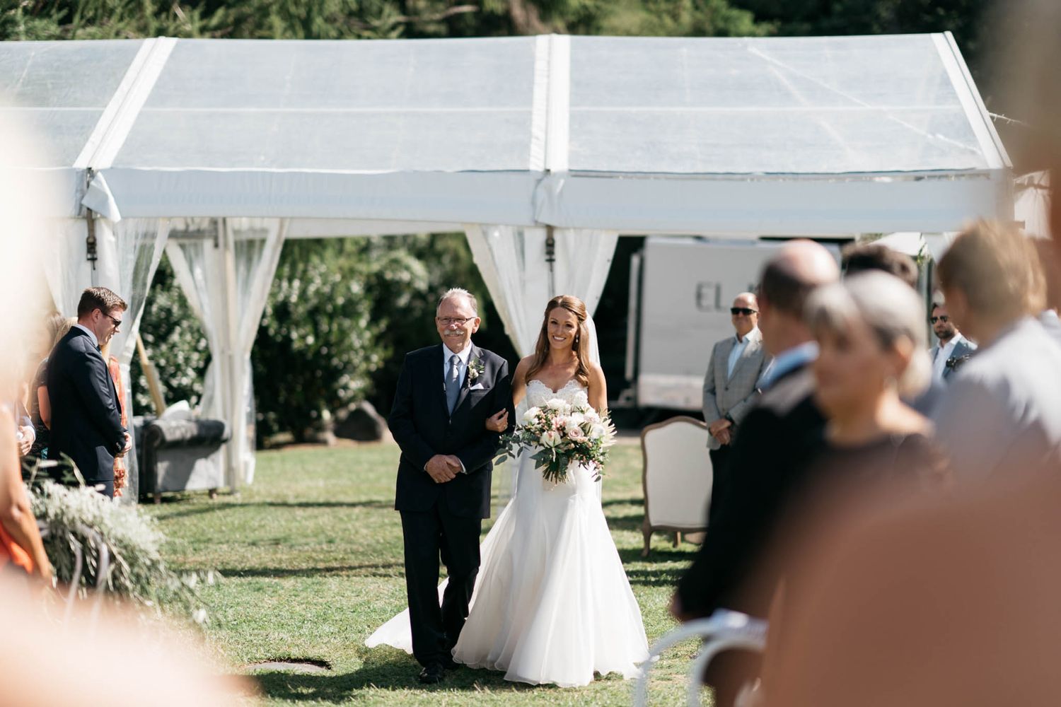An outdoor wedding ceremony under white tents with guests gathered on a sunny grassy lawn at a plantation estate.