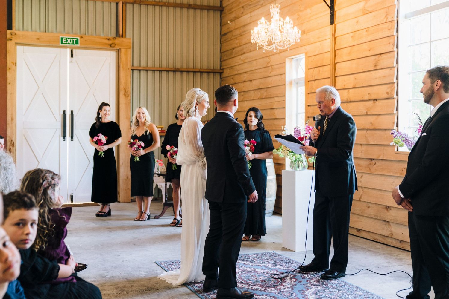 Modern rustic wedding venue interior with wooden walls and gathered guests awaiting ceremony.