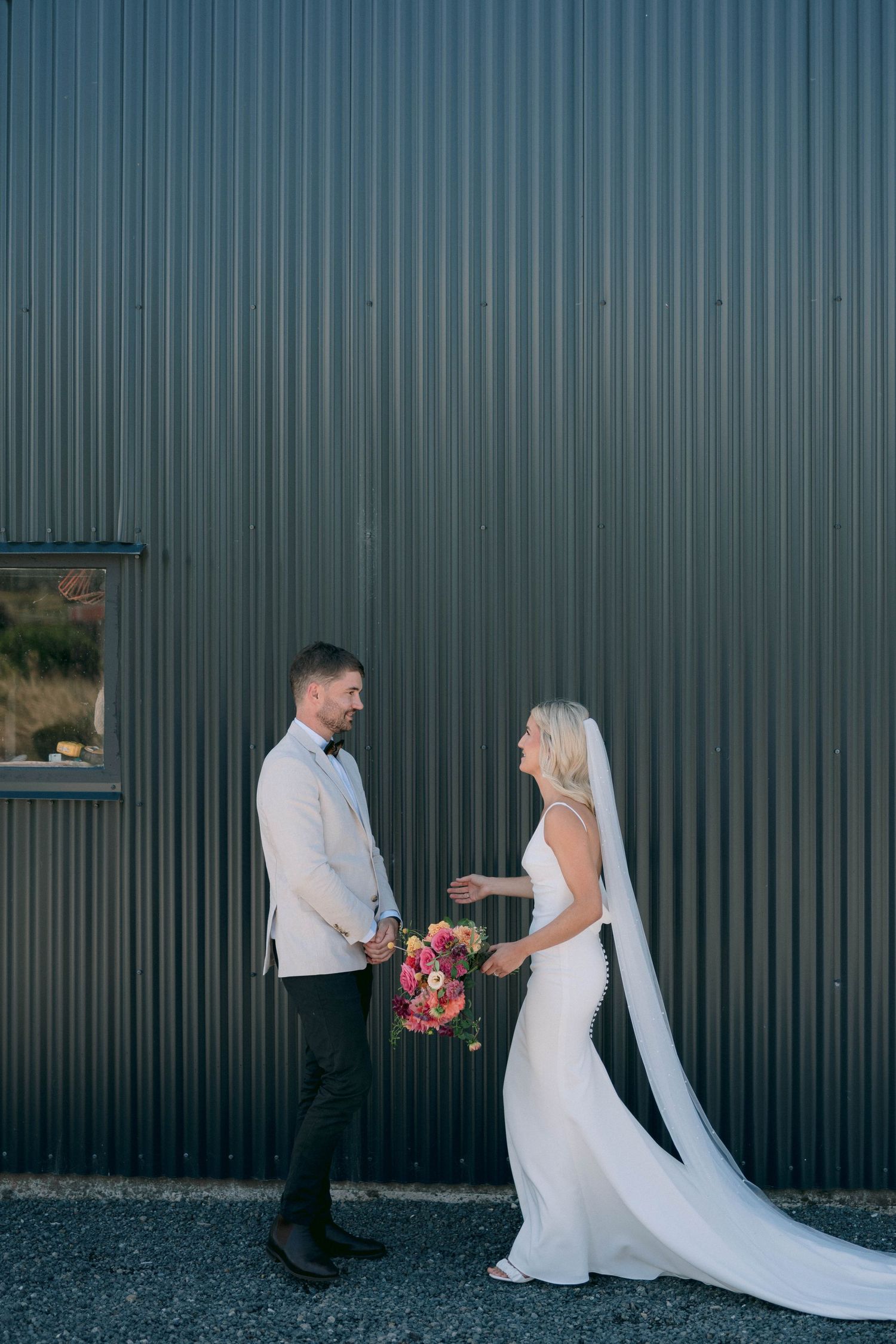 A wedding couple shares a joyful moment against a modern green corrugated metal wall.