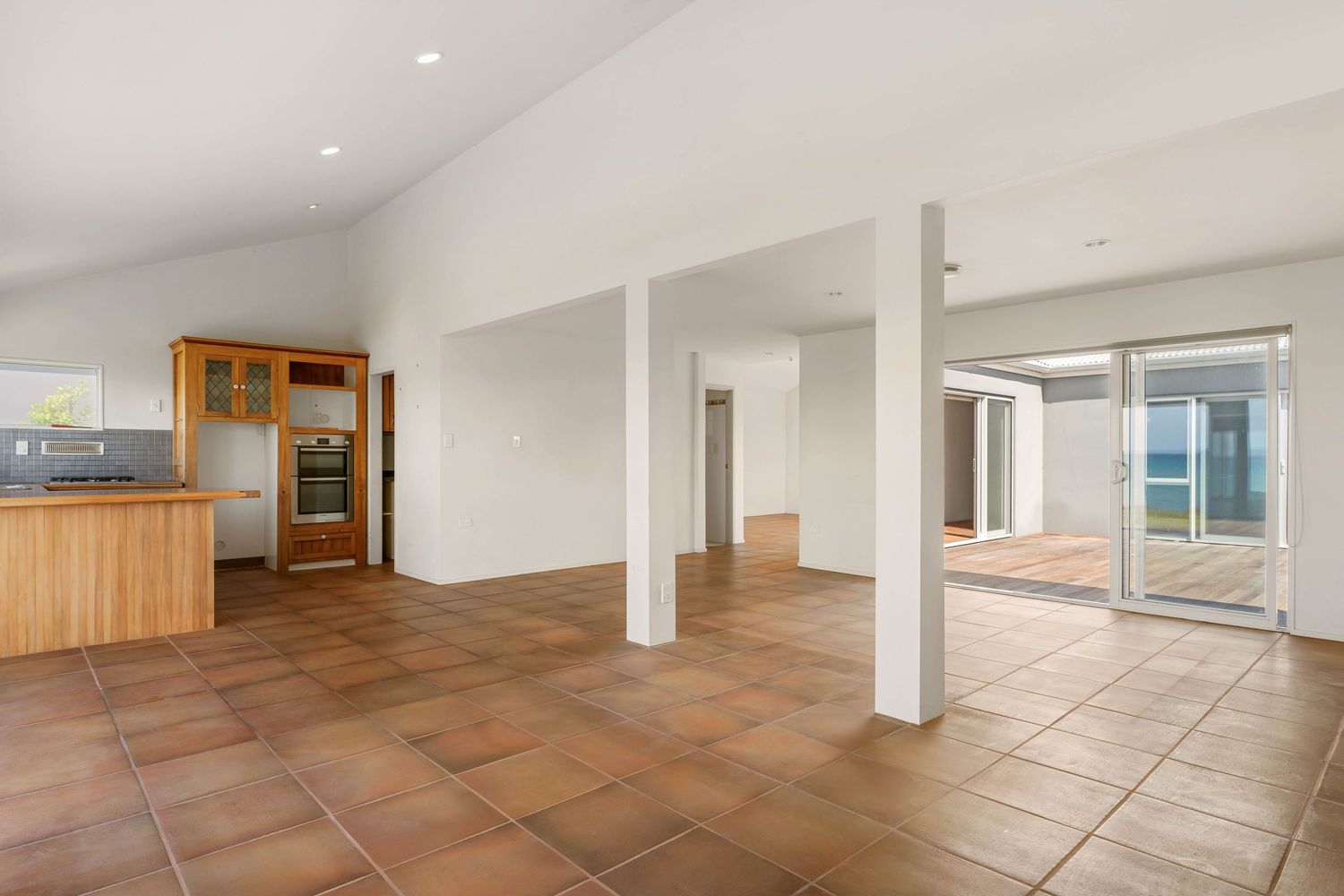 Modern open floor plan interior featuring terracotta tiles, white columns, and wood cabinets in the kitchen area.