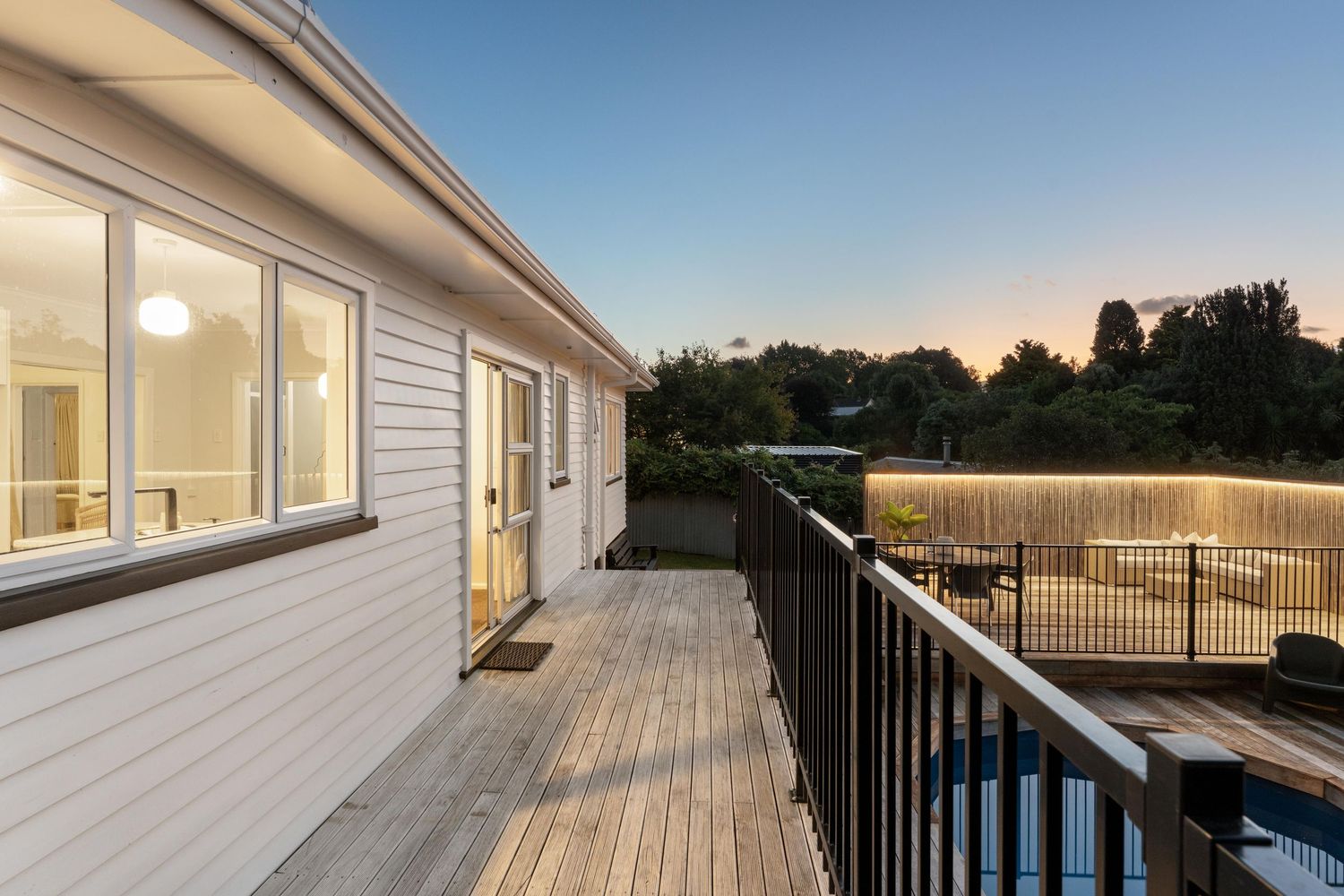 Exterior view of a modern home with large deck and pool area during sunset.