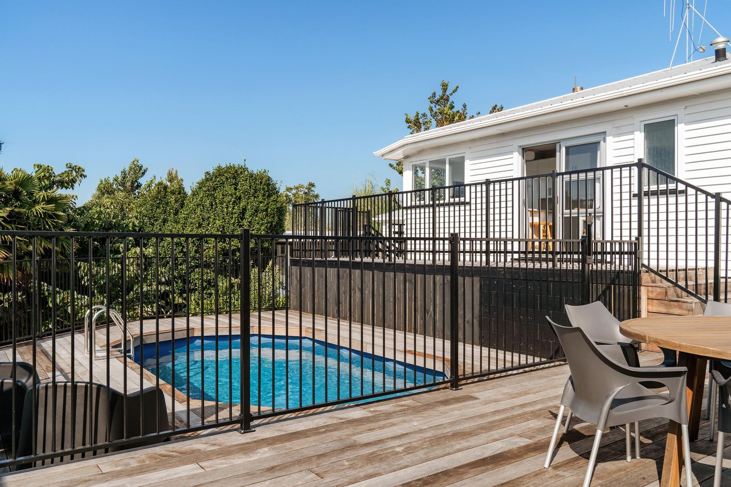 Long wooden deck with black metal railing overlooking swimming pool and landscaped yard.