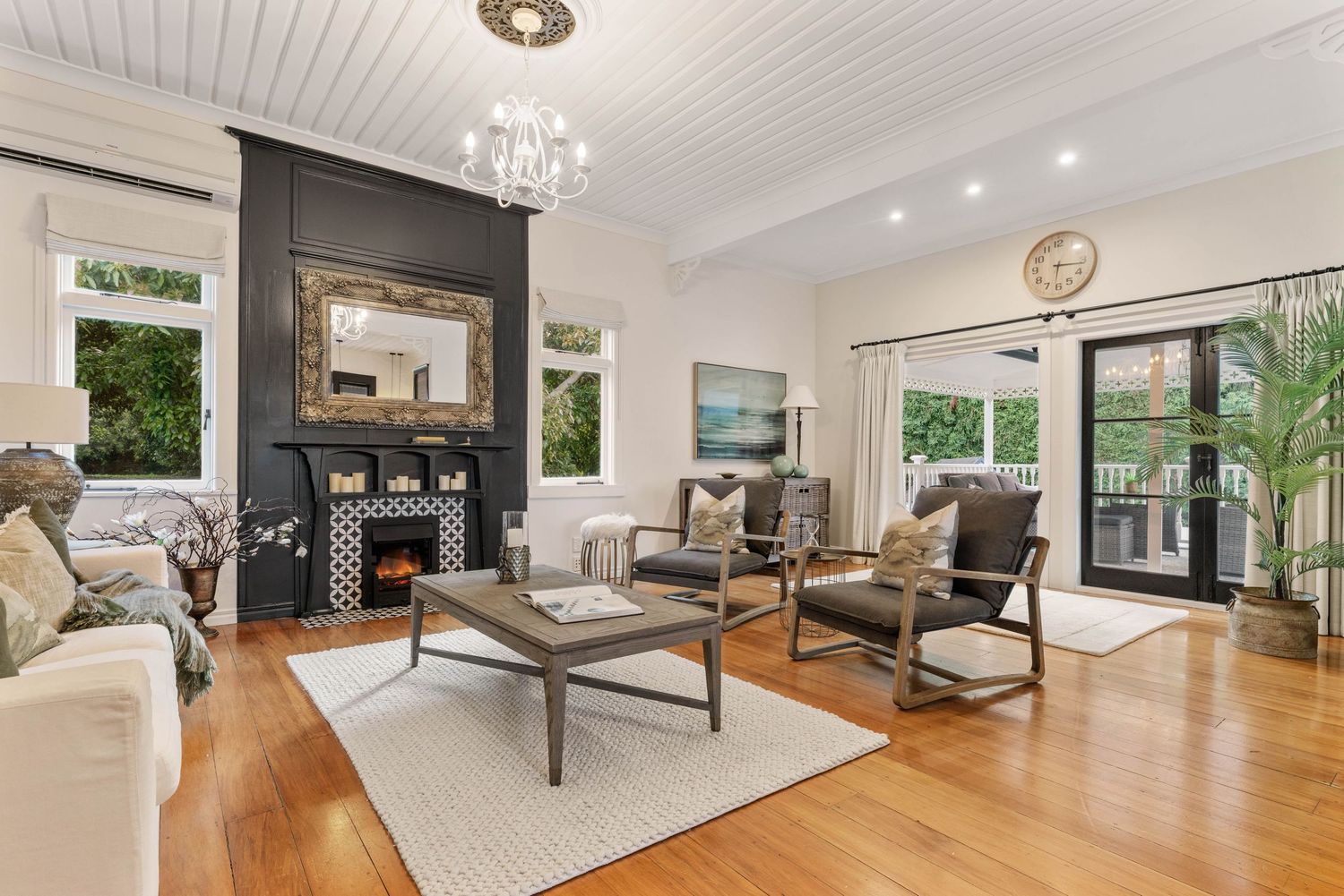 Modern living room with black fireplace wall, hardwood floors, and crystal chandelier in bright airy space.