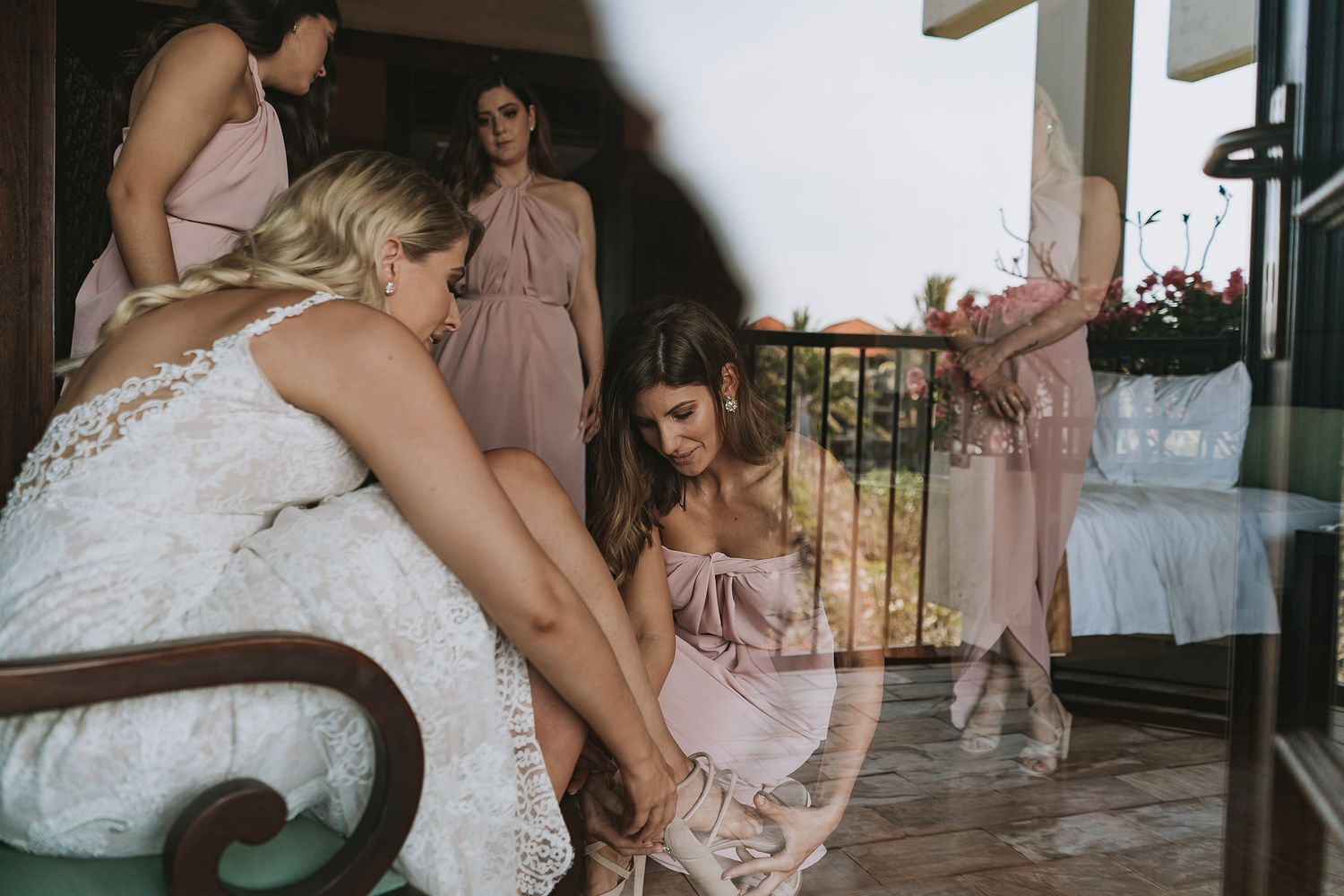 Bridesmaids in pink dresses assist the bride getting ready on her wedding day.