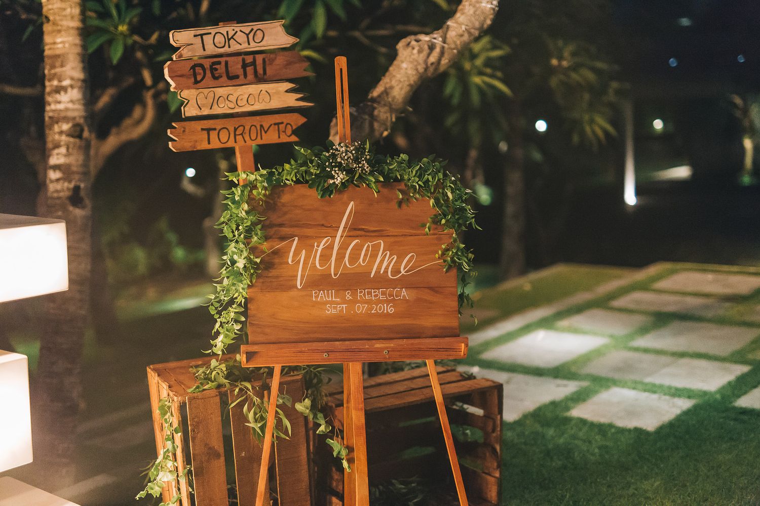 Rustic wooden wedding welcome signs decorated with greenery at outdoor reception.
