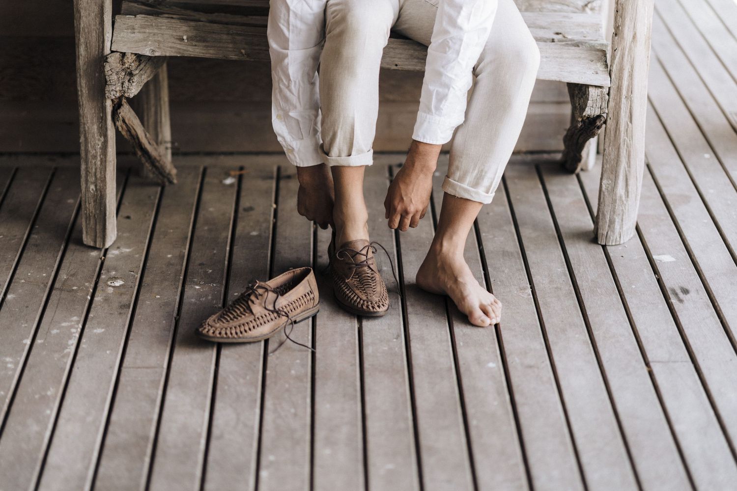 Close-up view of light brown boat shoes on wooden deck floor with white pants.