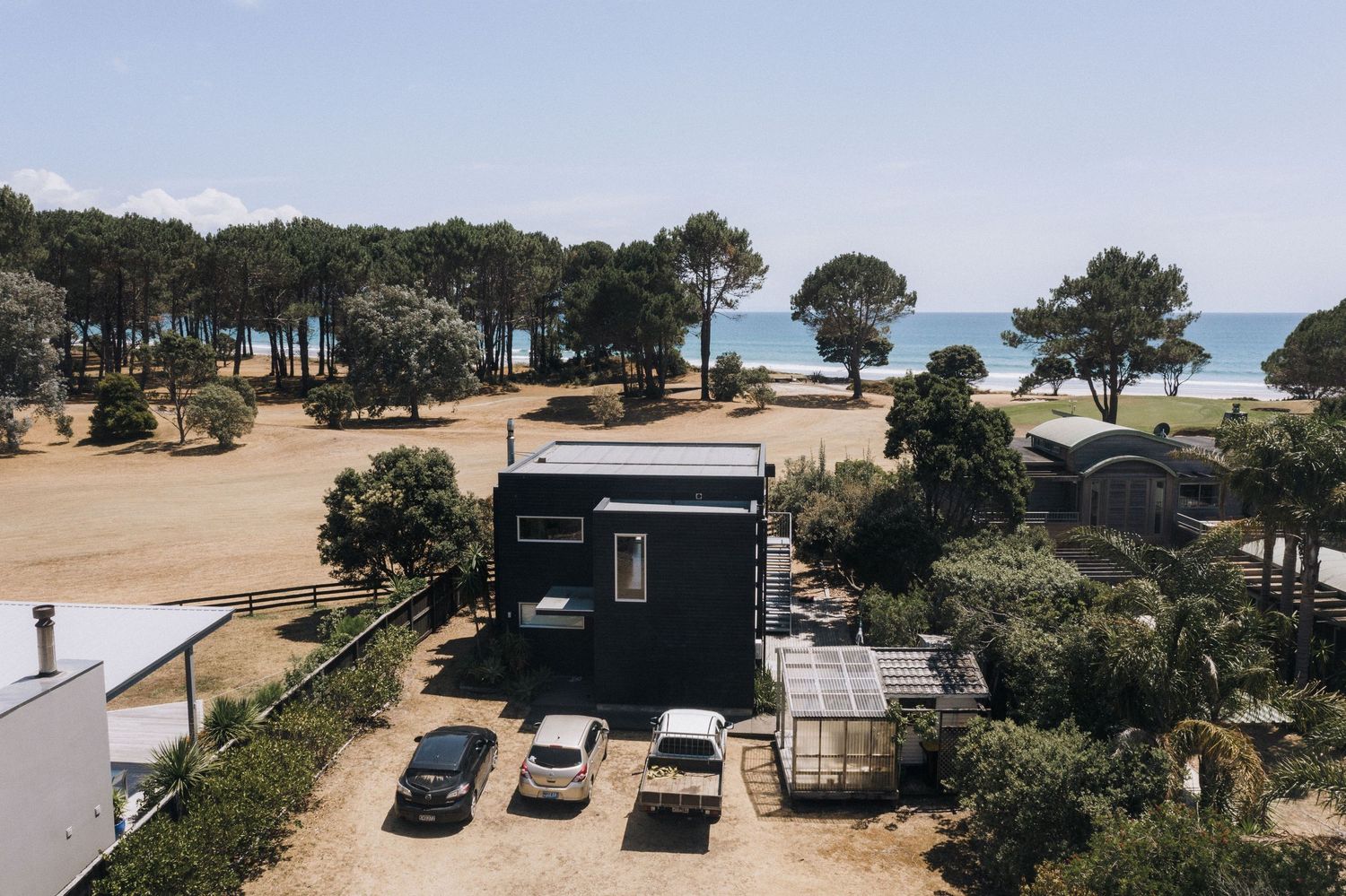 Aerial view of a black food truck parked near the beach with trees and ocean in the background.